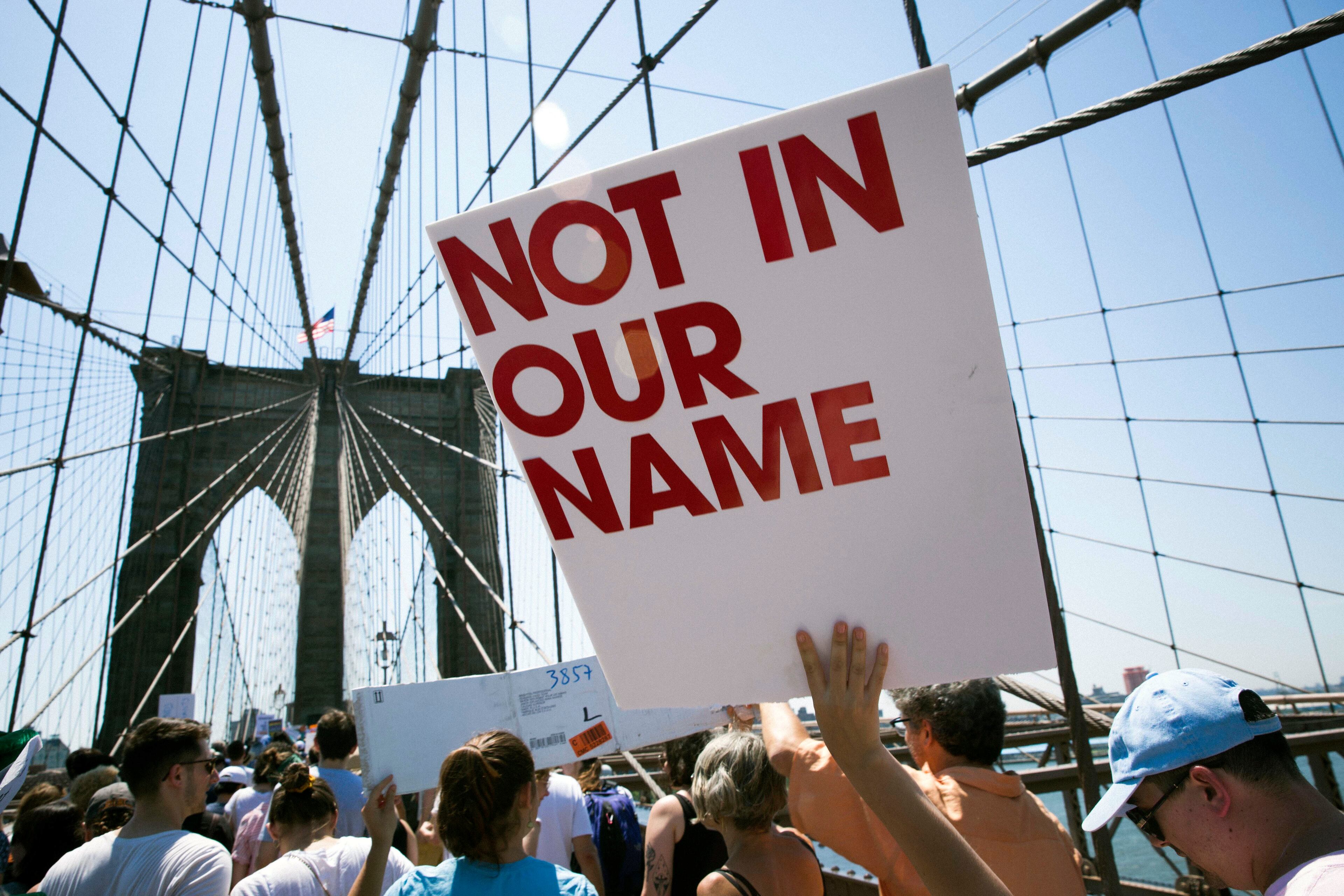 Activists carry signs across the Brooklyn Bridge during a rally to protest the Trump administration's immigration policies Saturday, June 30, 2018, in New York, New York. (AP Photo/Kevin Hagen)