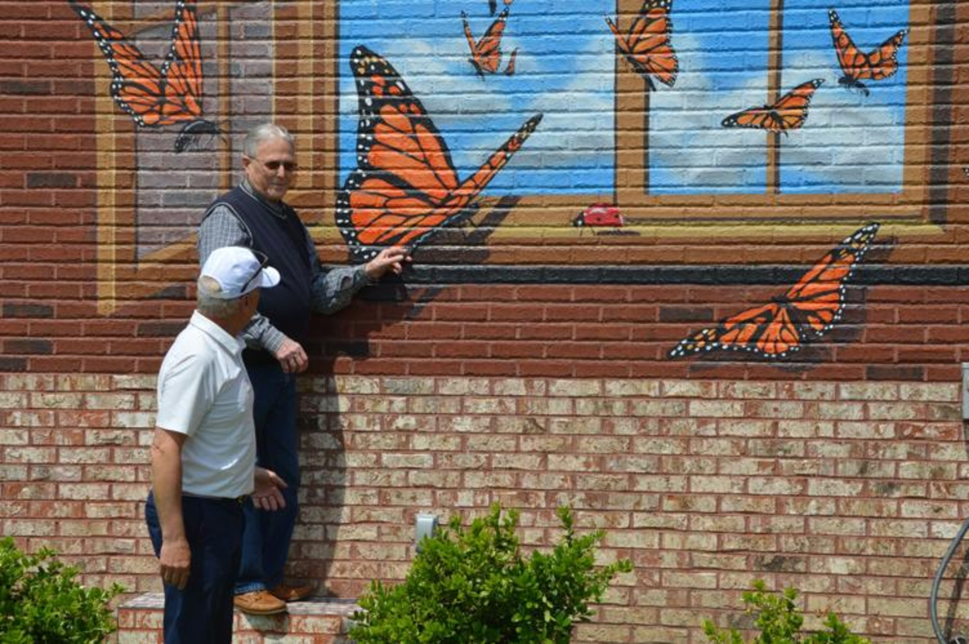 Lilburn Mayor Johnny Crist shows Jim Scruggs how to interact with a butterfly mural at City Park during a tour around Old Town Lilburn. (Photo Courtesy of Curt Yeomans/Gwinnett Daily Post)
