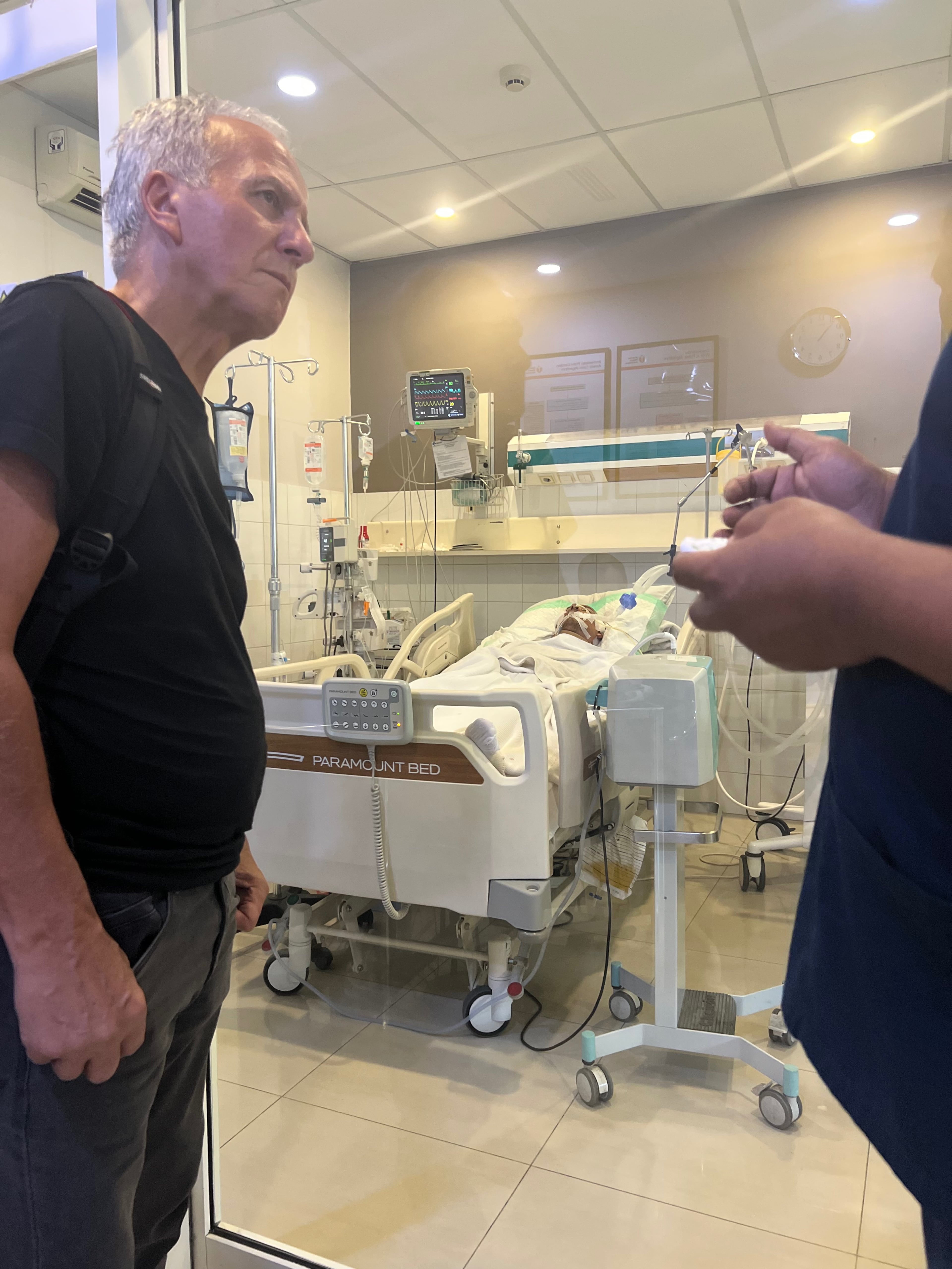 Jan Moczarski stands in front of his son Mark Moczarski, who remains in a coma in Bali as the family works to get him home. (Family photo)