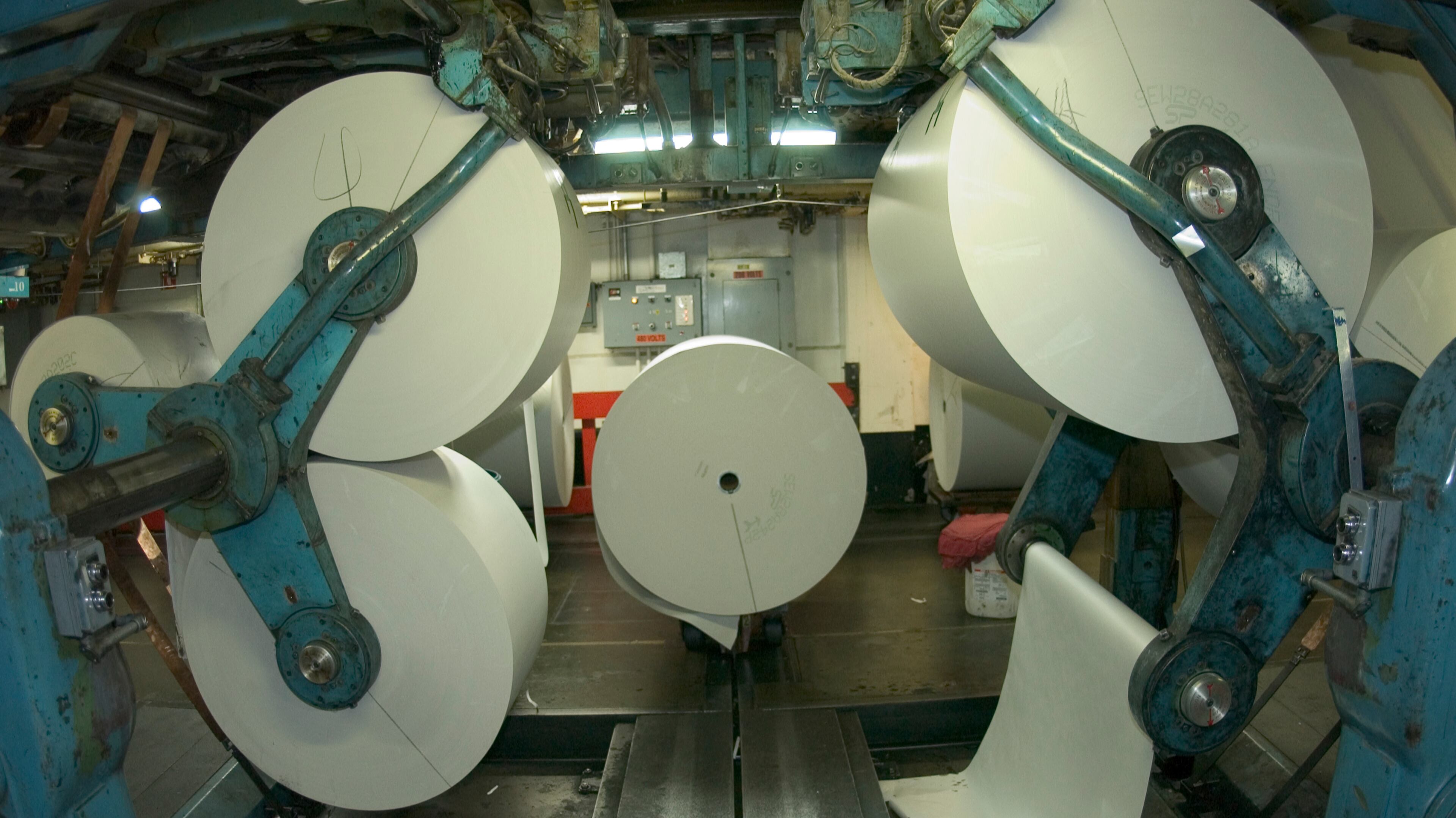 Large rolls of newsprint on tracks and spindles, prepared for printing. Canadian newsprint now carries hefty tariffs. AJC file