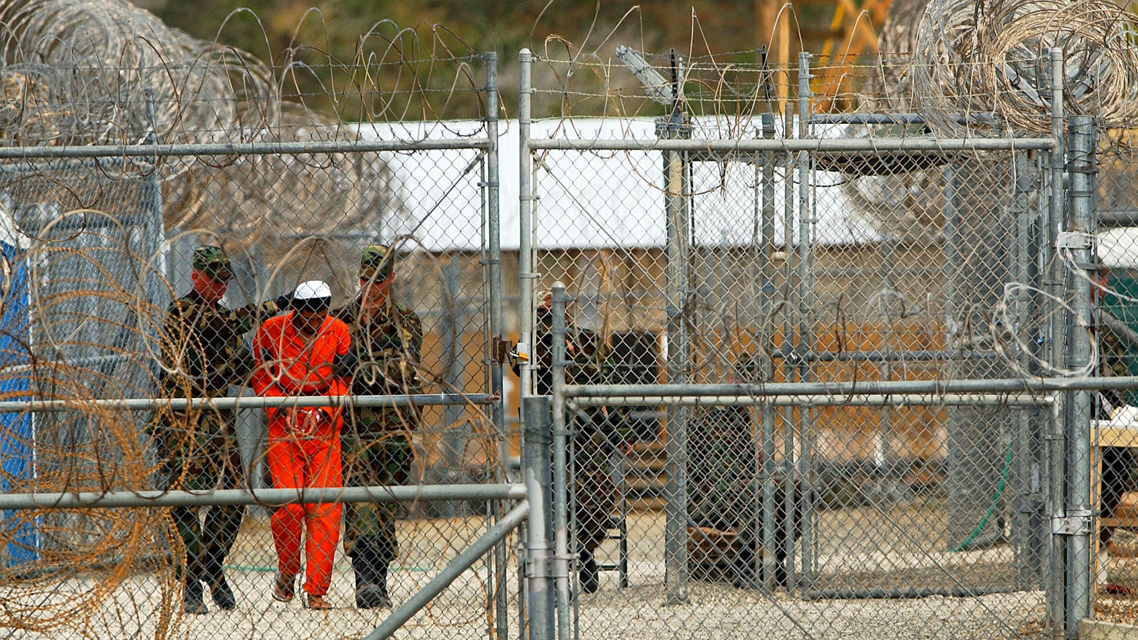 Marines transport a detainee behind layers of fencing and razorwire in Camp X-Ray February 6, 2002 in Guantanamo Bay, Cuba. (Photo by Chris Hondros/Getty Images)