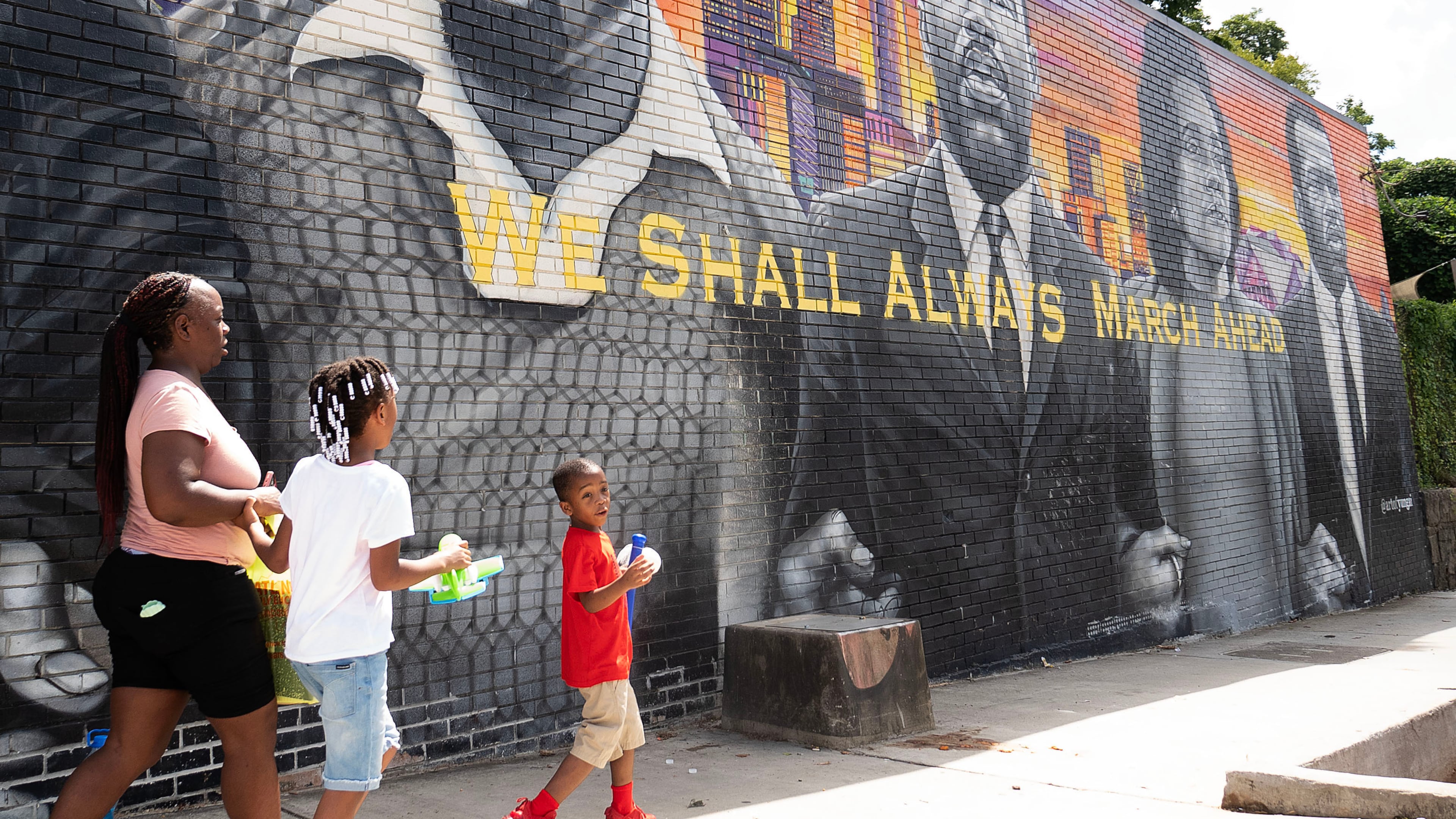 July 13, 2020, Atlanta — A family walks pass a mural on the side of Privado Barbershop in Vine City. The owner, Samuel Glickman, opened his shop up for “The Confess Project,” an organization that enlists barbershops like Privado to double as mental health centers, where Black men can comfortably talk about their issues. (RYON HORNE/RHORNE@AJC.COM)