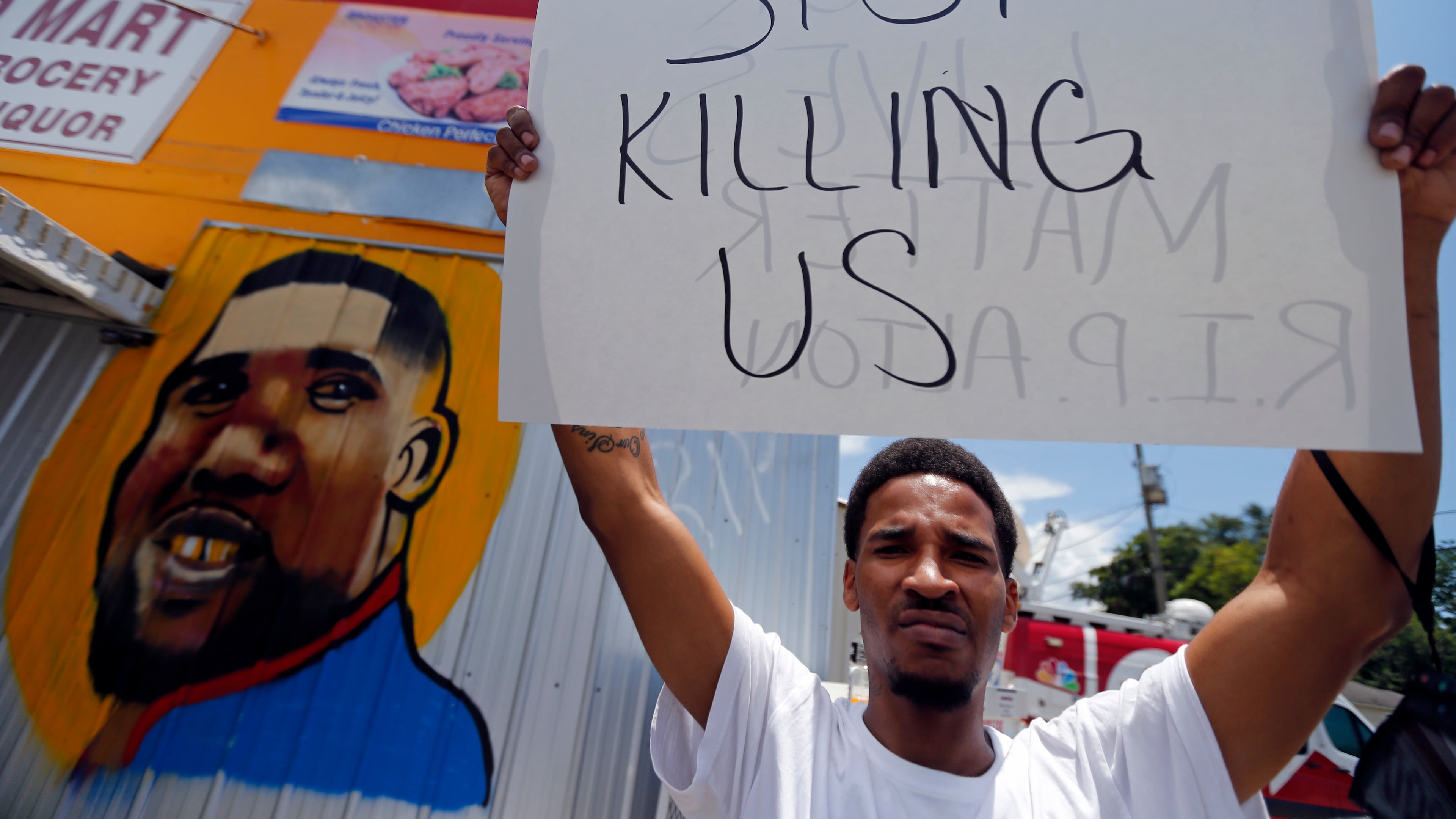 A man holds a sign in front of a mural of Alton Sterling while attorneys, not pictured, speak in front of the Triple S Food Mart in Baton Rouge, La., Thursday, July 7, 2016. Sterling, 37, was shot and killed outside the convenience store by Baton Rouge police, where he was selling CDs. (AP Photo/Gerald Herbert)