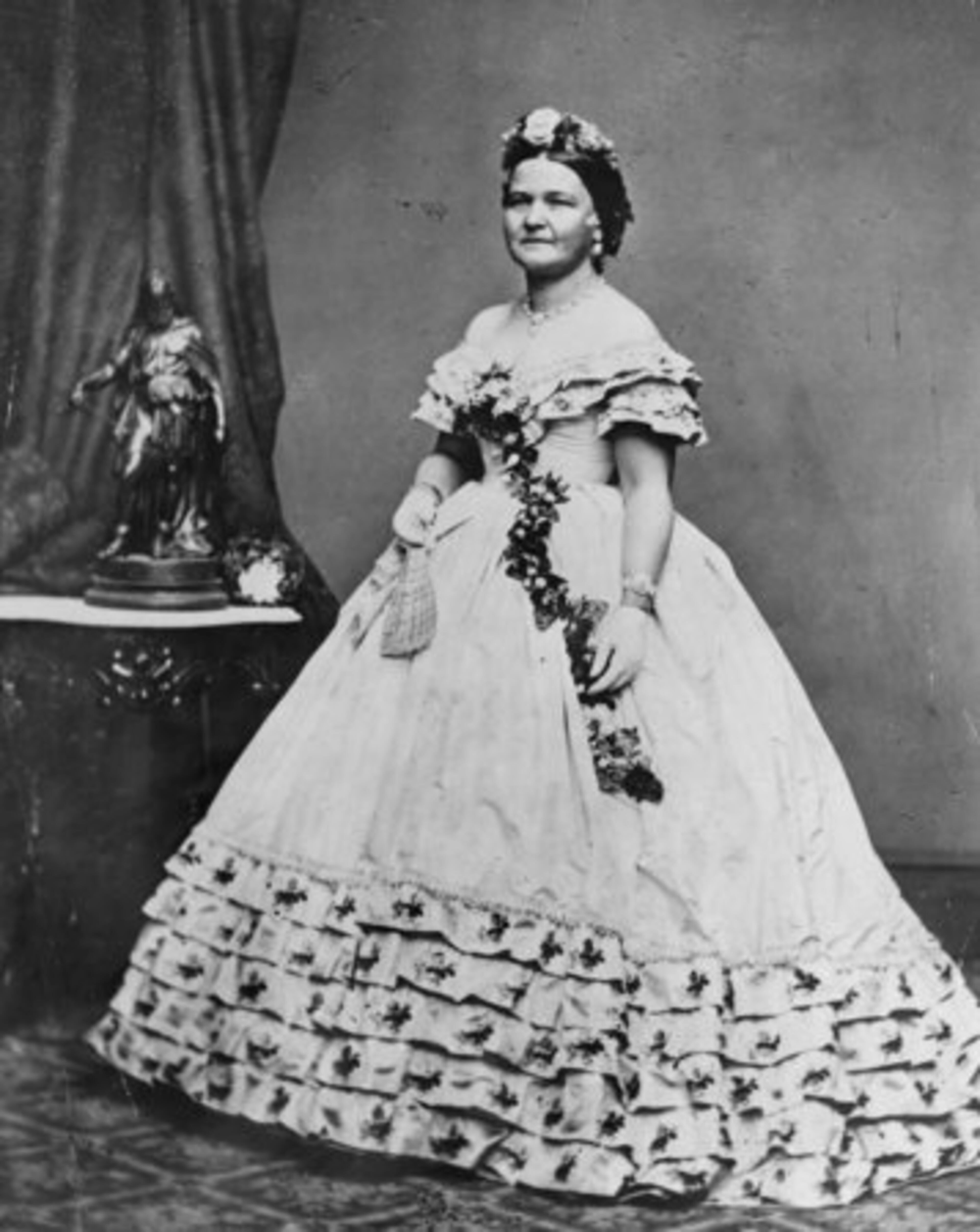 In 1861, Mary Todd Lincoln hoped her lavish clothing would squash Washington society's doubts about her social graces, but the massive off-the-shoulder, floral embroidered gown with three tiers of ruffles at the bodice, along with the flowers in her hair, made her appear as if she were trying too hard.