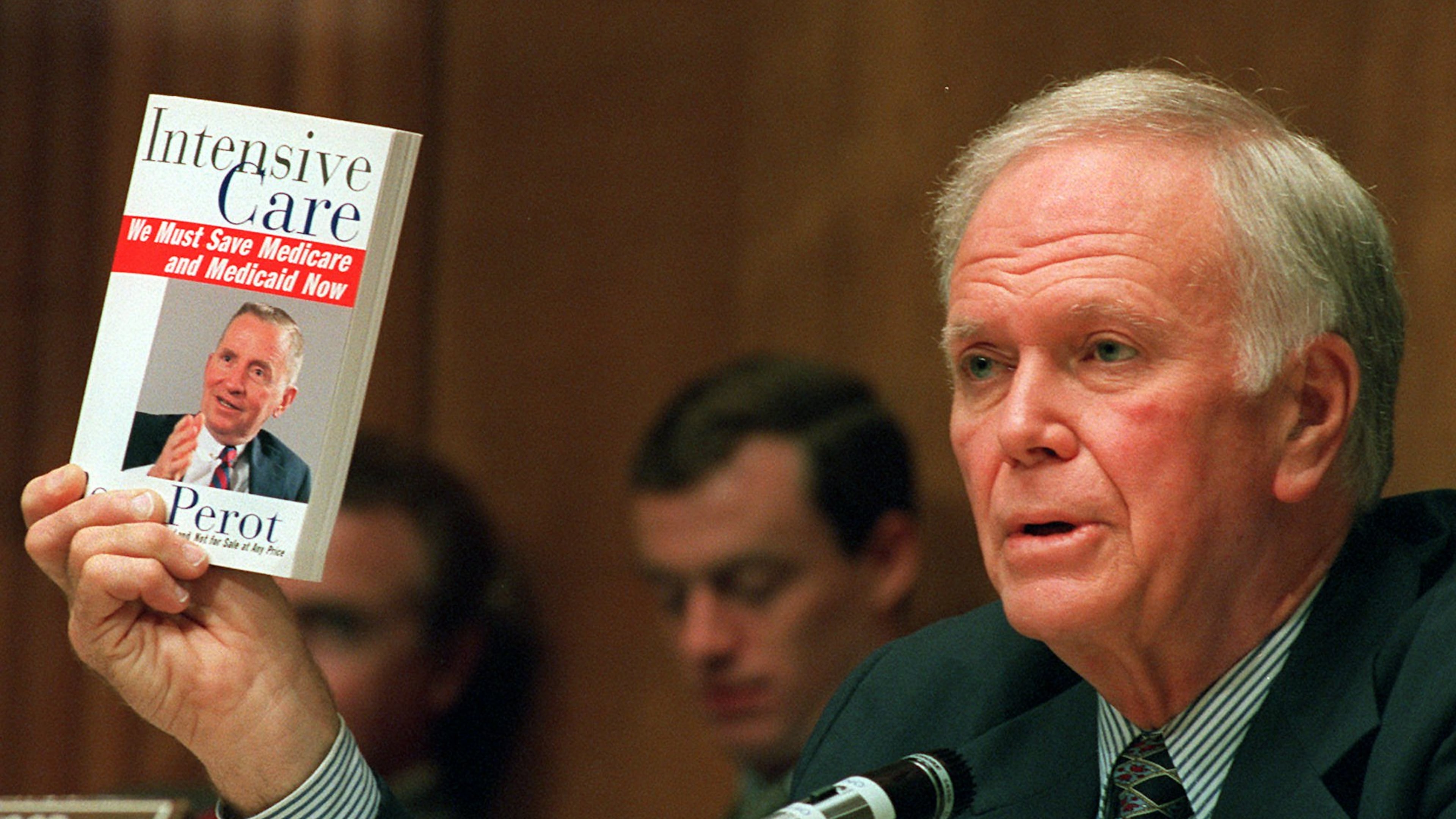 FILE - Senate Finance Committee Chairman Bob Packwood, R-Ore., holds a book entitled "Intensive Care" by Ross Perot, during hearings dealing with the future of Medicare on Capitol Hill, Aug. 30, 1995. (AP Photo/Dennis Cook, File)