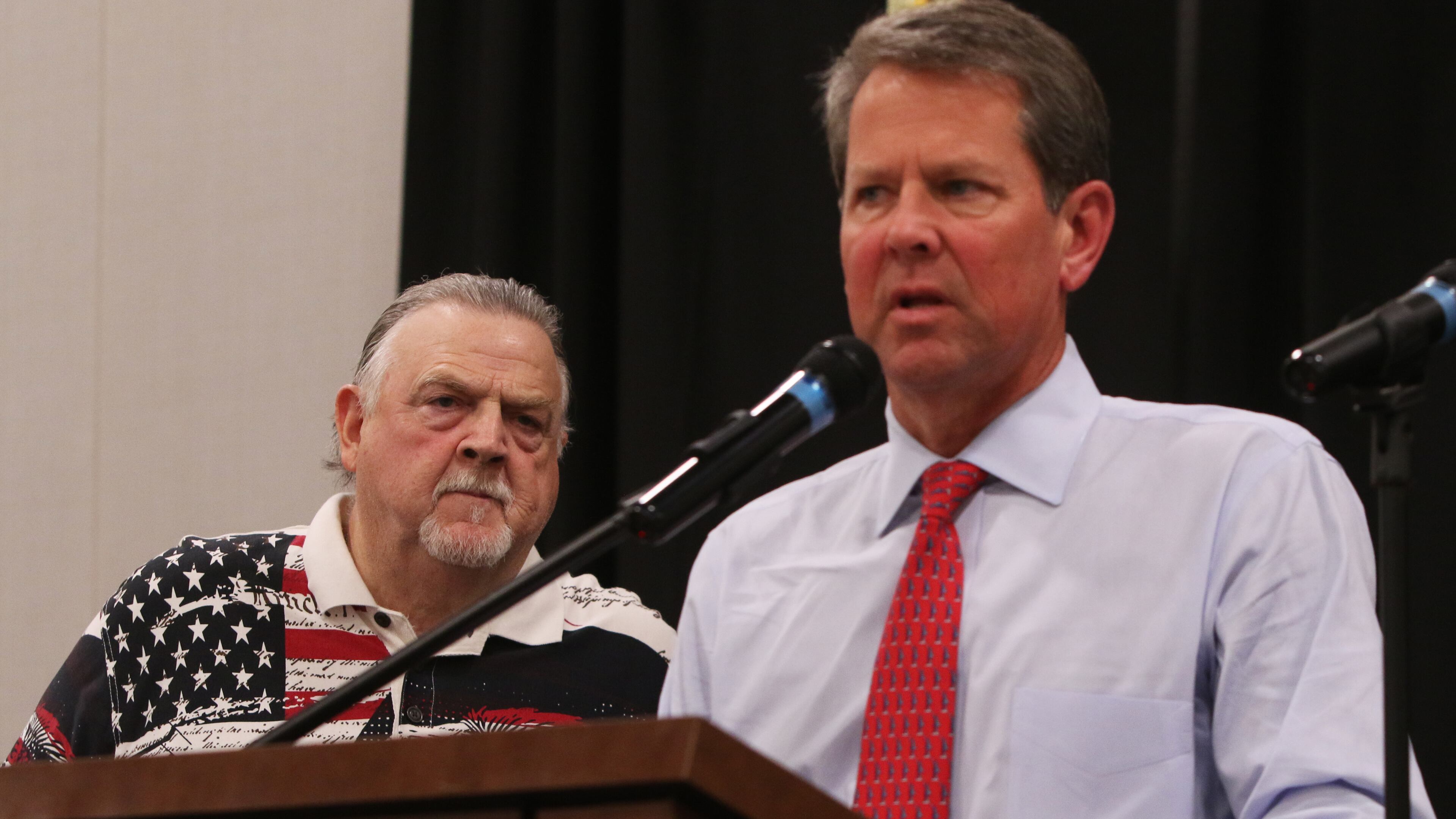 Cobb County Sheriff Neil Warren (left) looks on while Georgia Gov.r Brian Kemp (right) addresses the crowd during the 30th annual Cobb Sheriff's Corn Boilin' at Jim Miller Park in Marietta on Monday. Christina Matacotta/Christina.Matacotta@ajc.com
