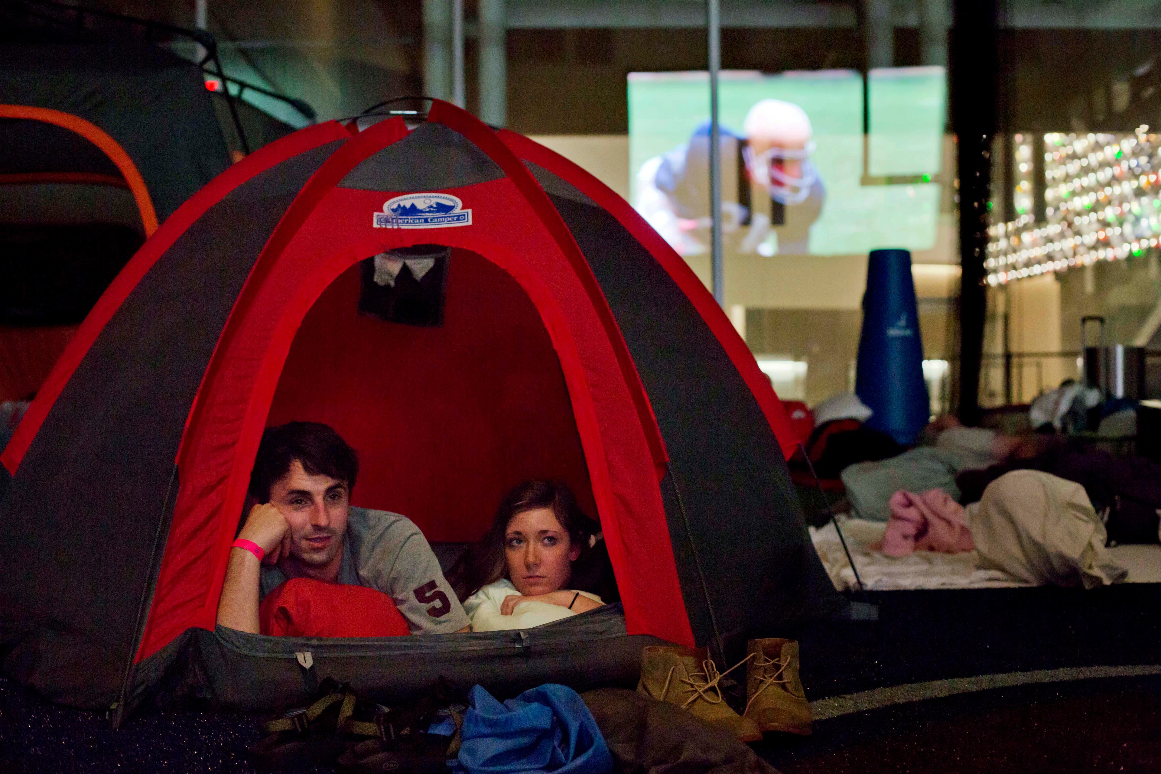 Michael Adams, left, of Kennesaw, Ga., and Anna Strohm, of Nashville, Tenn., watch from their tent as the movie "Rudy" is seen reflected off the glass while playing during a sleepover in the College Football Hall of Fame, Wednesday, Aug. 13, 2014, in Atlanta. One hundred contest winners who wrote an essay detailing their love of college football were selected to stay with a guest overnight in Atlanta�s College Football Hall of Fame before its grand opening and win a year�s supply of Chick-fil-A. (AP Photo/David Goldman)