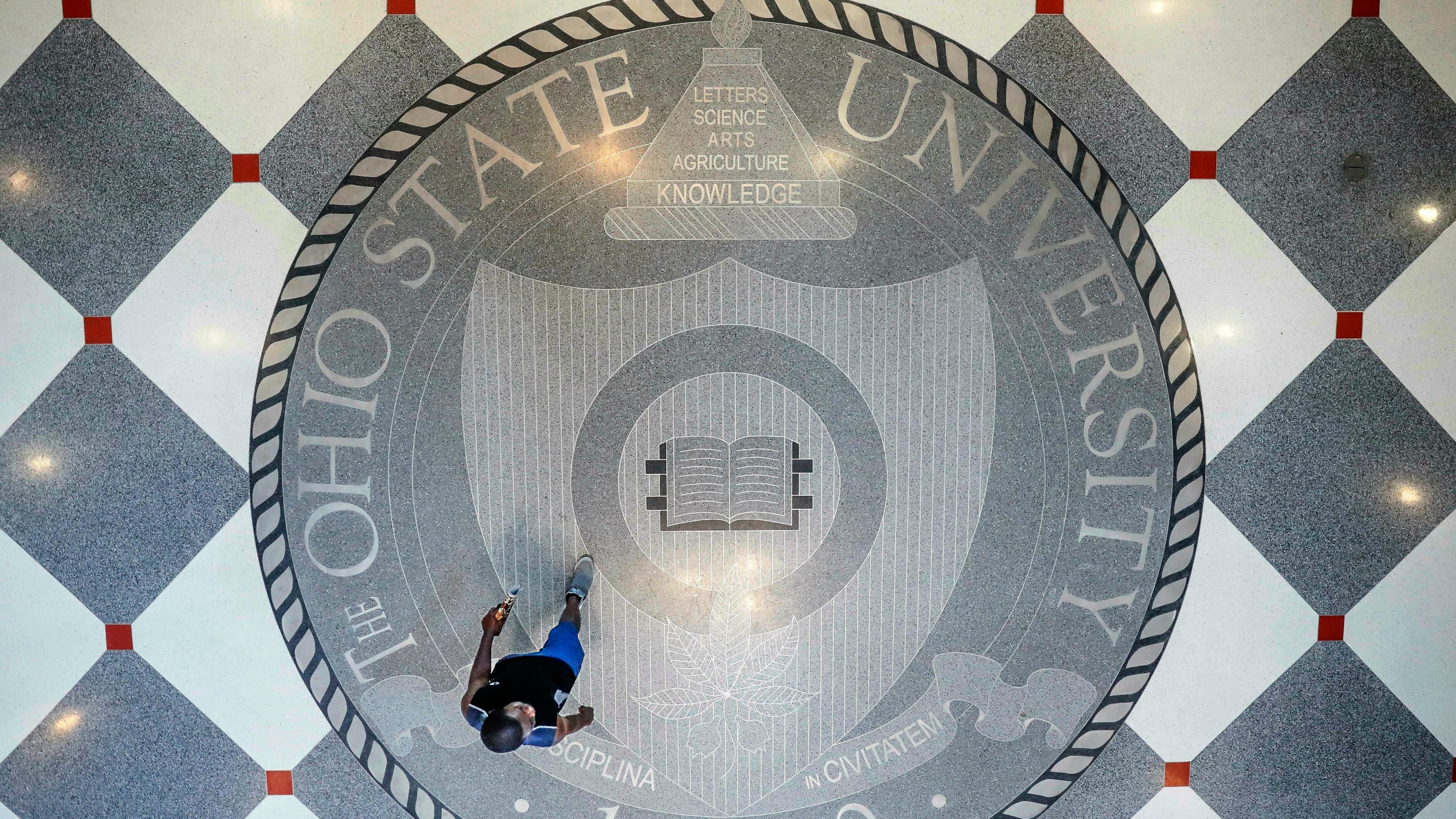 FILE - A person walks over the Ohio State University's emblem in the campus student union, May 18, 2019, in Columbus, Ohio. (AP Photo/John Minchillo, File)