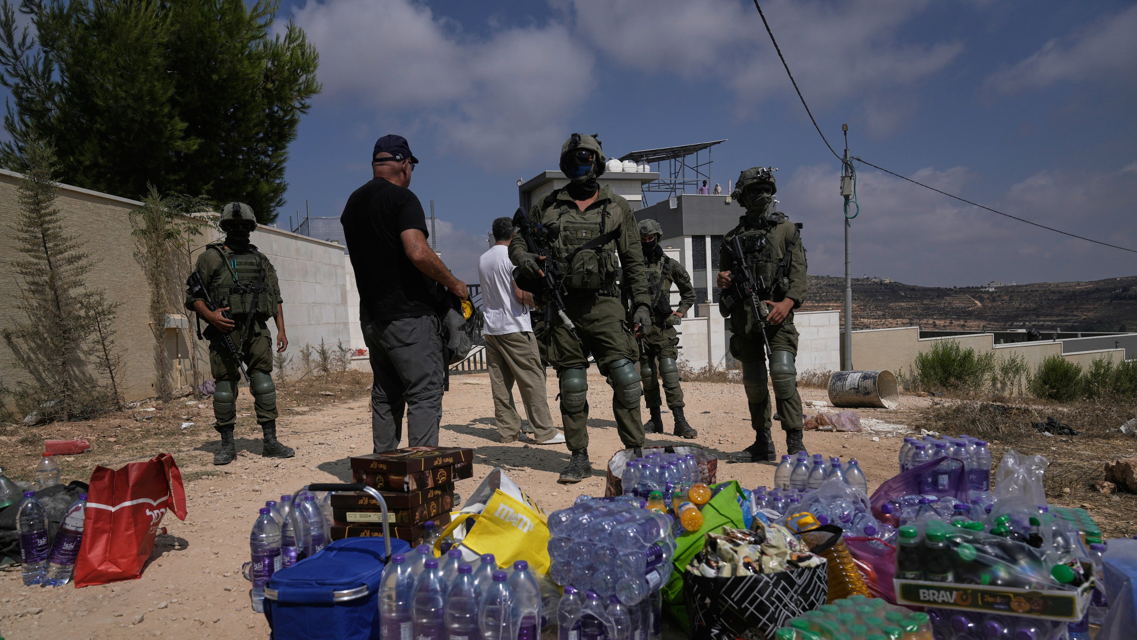 Activists accumulate food and water supplies in front of Israeli army soldiers who are blocking the road leading to the houses of three Palestinian families that have been besieged by Israeli settlers for six days, in the occupied West Bank village of Qusra, south of Nablus, Friday, Aug. 14, 2026. (AP Photo/Majdi Mohammed)