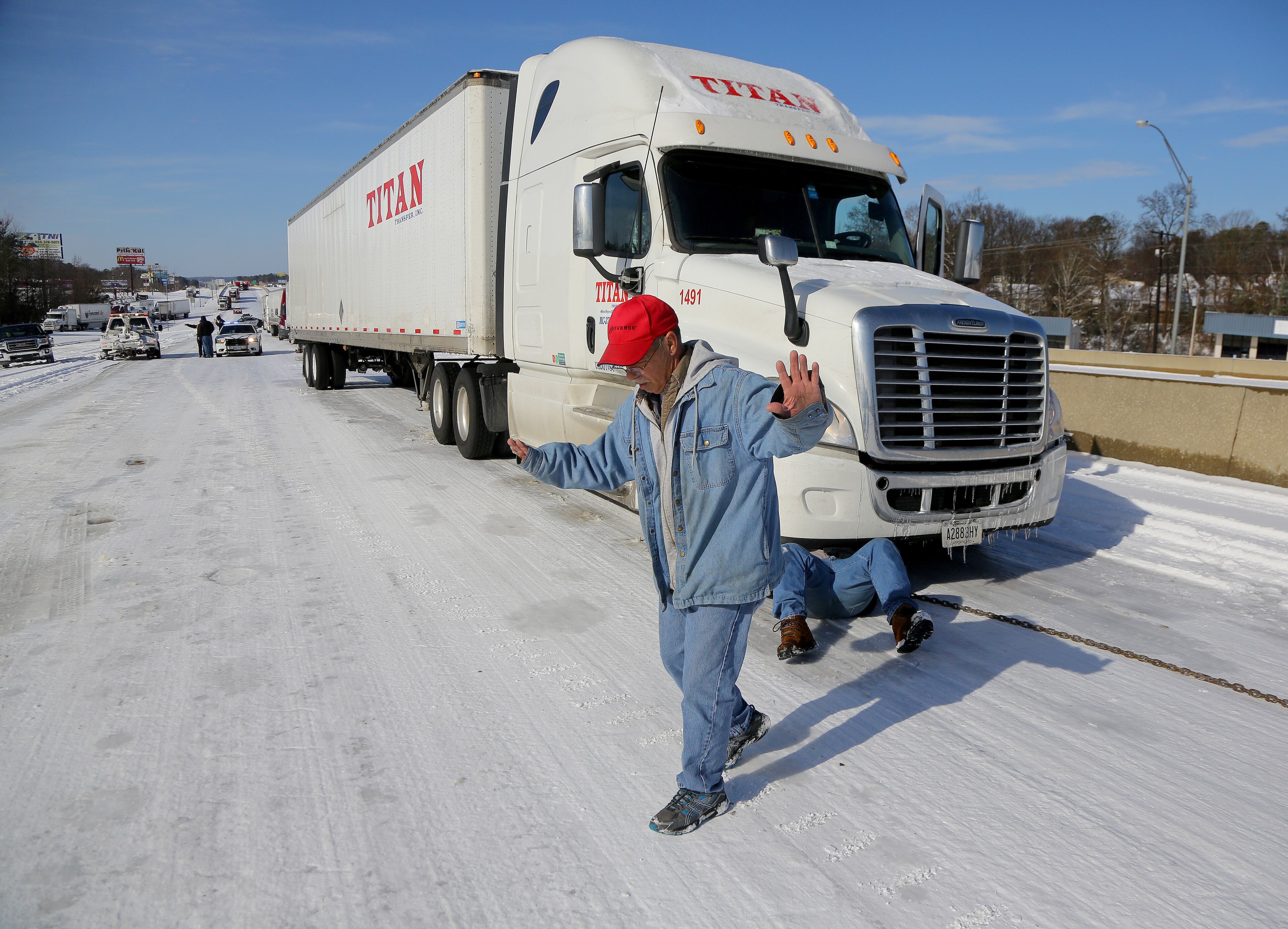 Trucker William Booneyham, stretches his arms out for balance as he walks across an ice-packed Interstate 30, Thursday morning, March 5, 2015, as tow operator William Bowden, right, hooks up to pull Booneyham's truck up an incline at mile marker 118 in Benton, Ark. Booneyham's truck and many others along I-30 became stuck on slight uphills when they had to slow for traffic or other wrecks, backing up traffic for miles. (AP Photo/The Arkansas Democrat-Gazette, Stephen B. Thornton) ARKANSAS TIMES OUT; ARKANSAS BUSINESS OUT