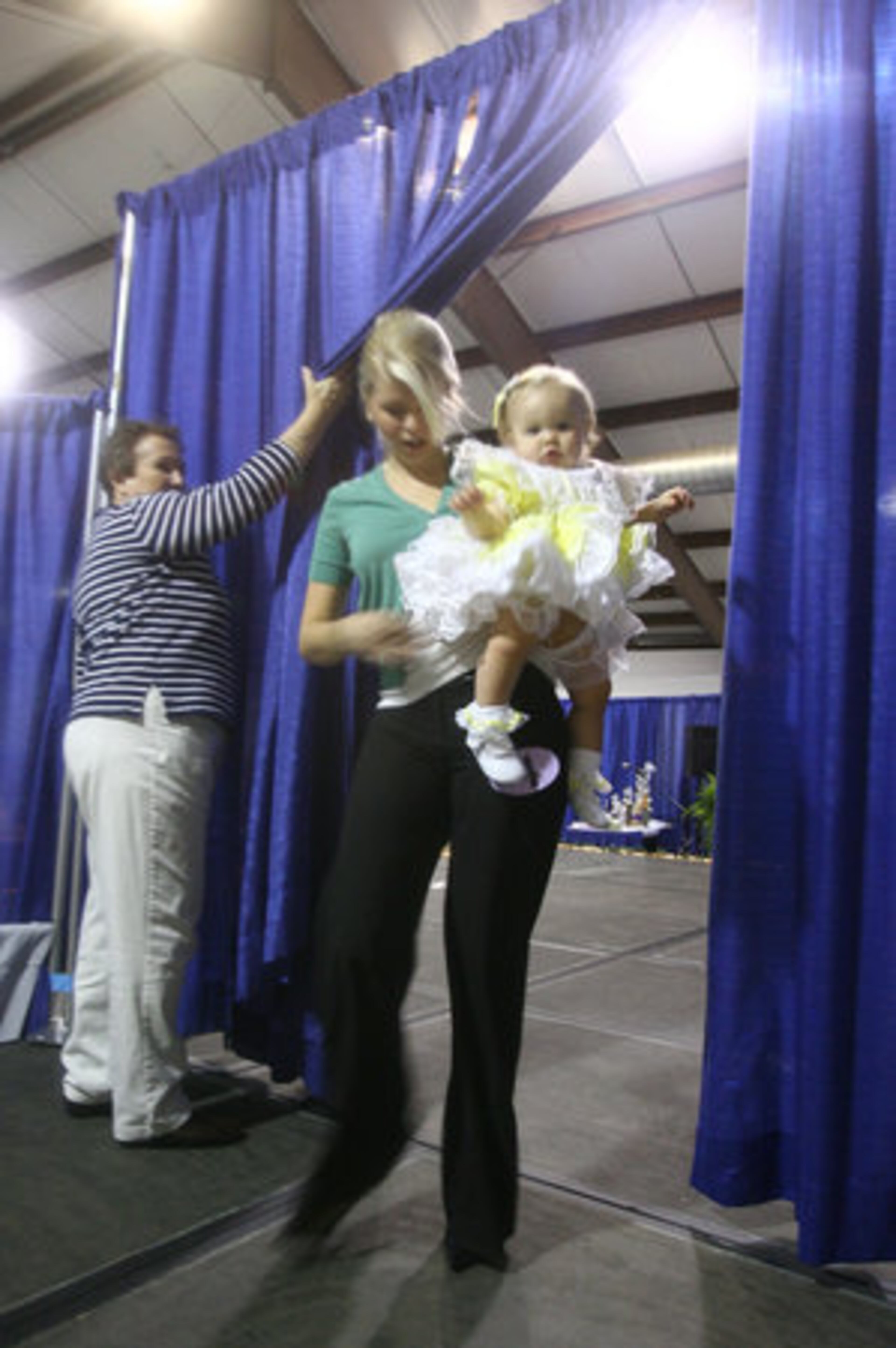 Connie Baughman, a board member for the Miss Gwinnett County Scholarship Pageant, holds the curtain for Katy Kelley of Winder and her daughter, Ashlyne Kelley, 10 months, who latery won first runner-up in the baby pageant. Many of the mothers and a grandmother who escorted their contestants seemed more nervous than their babies.