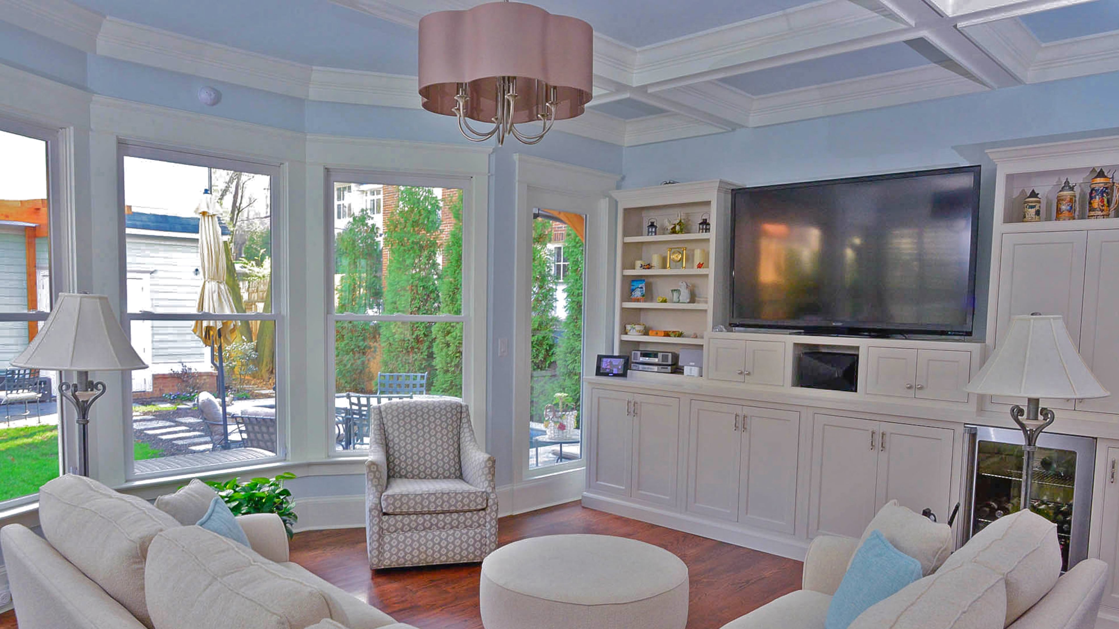 Built-in bookshelves and a sectional wrap around the great room. The shelves were designed to accommodate the flat-screen TV from their previous home.The coffered ceiling adds dimension while the expansive open windows offer a view to the backyard.