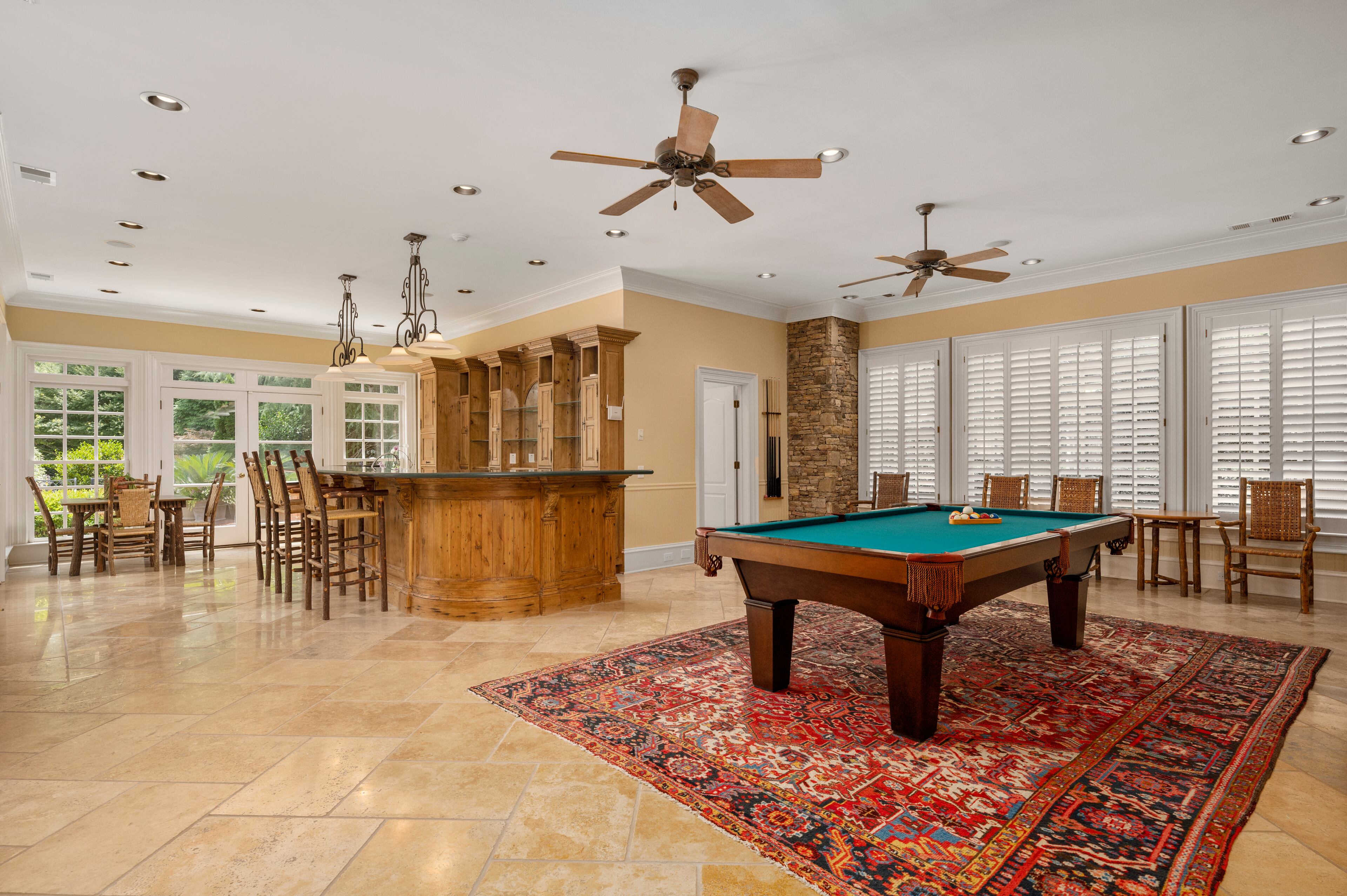 Oversized billiard/rec space with stone accent walls and travertine flooring leads to covered porch and offers a full pool bath with changing room and outdoor access. Text by Mallory Schrampfer