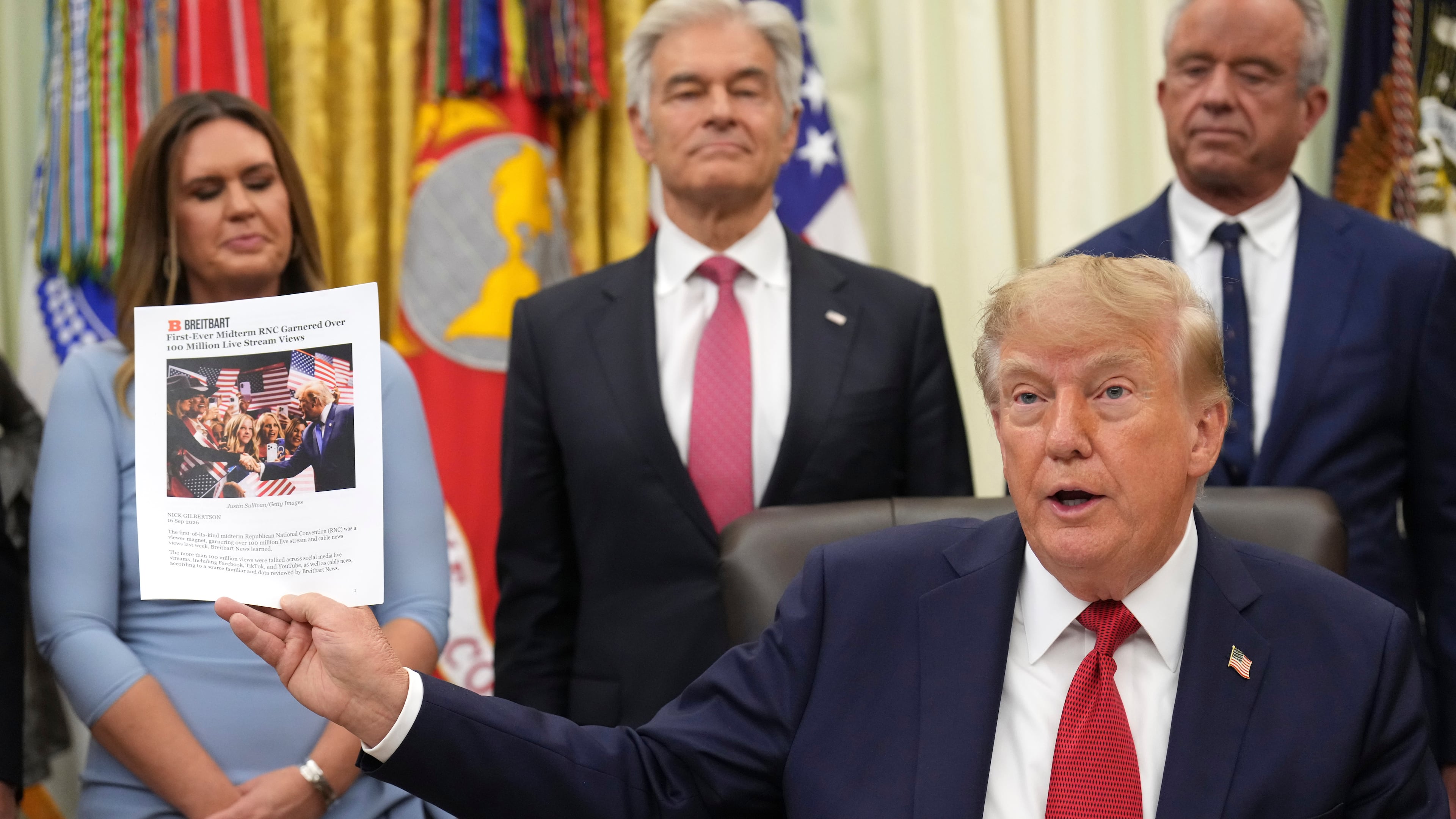 President Donald Trump holds up a printout of a Breitbart article as Arkansas Gov. Sarah Huckabee Sanders, from left, Mehmet Oz, administrator of the Centers for Medicare & Medicaid Services, and Health and Human Services Secretary Robert F. Kennedy Jr., look on during an event about healthcare in the Oval Office of the White House, Friday Sept. 18, 2026, in Washington. (AP Photo/Jacquelyn Martin)