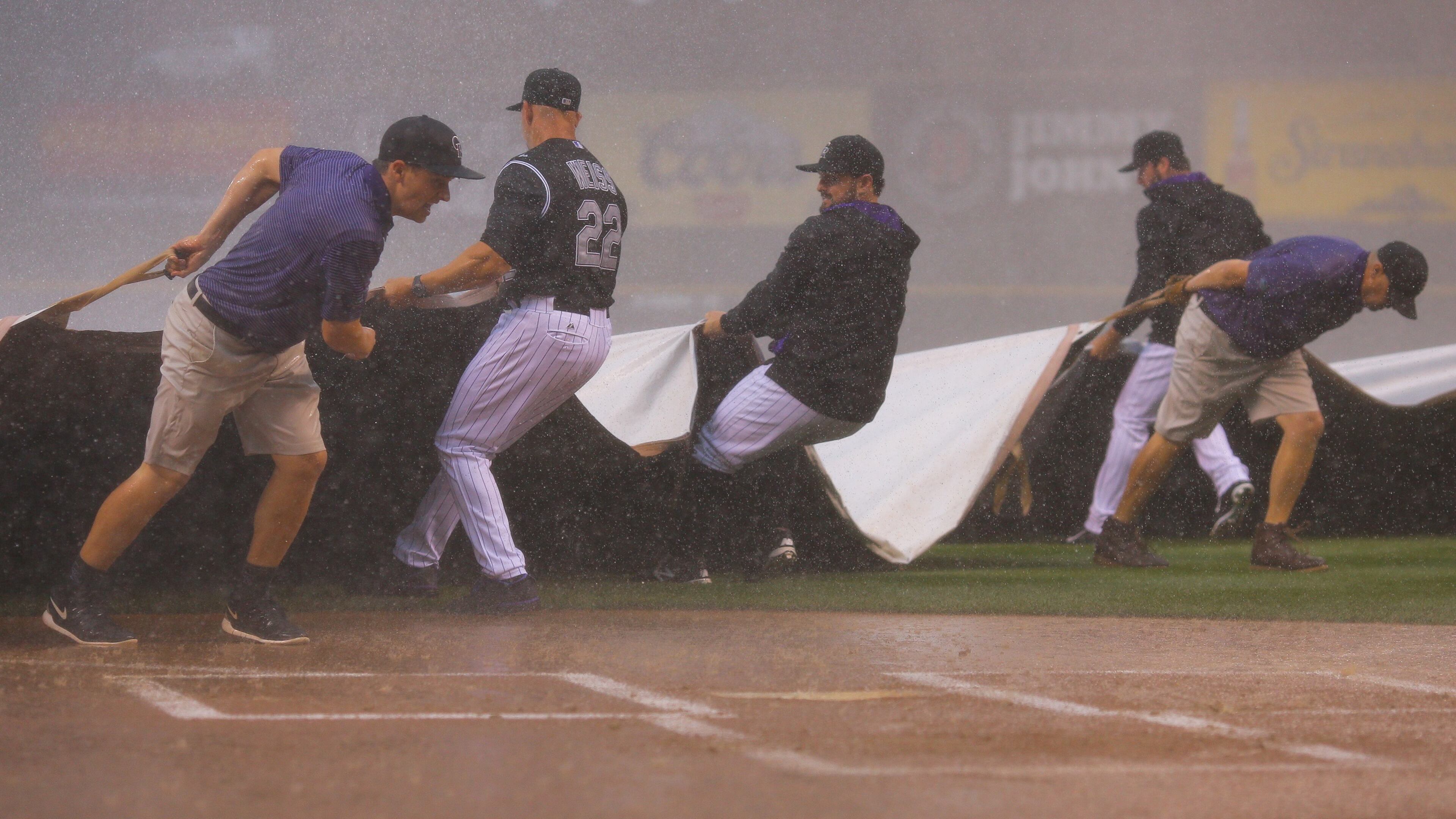 Manager Walt Weiss, catcher Michael McKenry #8 and starting pitcher Chad Bettis #35 of the Colorado Rockies help the grounds crew pull the tarp over the field during a could burst that halted play against the Atlanta Braves in the first inning at Coors Field on July 9, 2015 in Denver, Colorado. (Photo by Justin Edmonds/Getty Images)