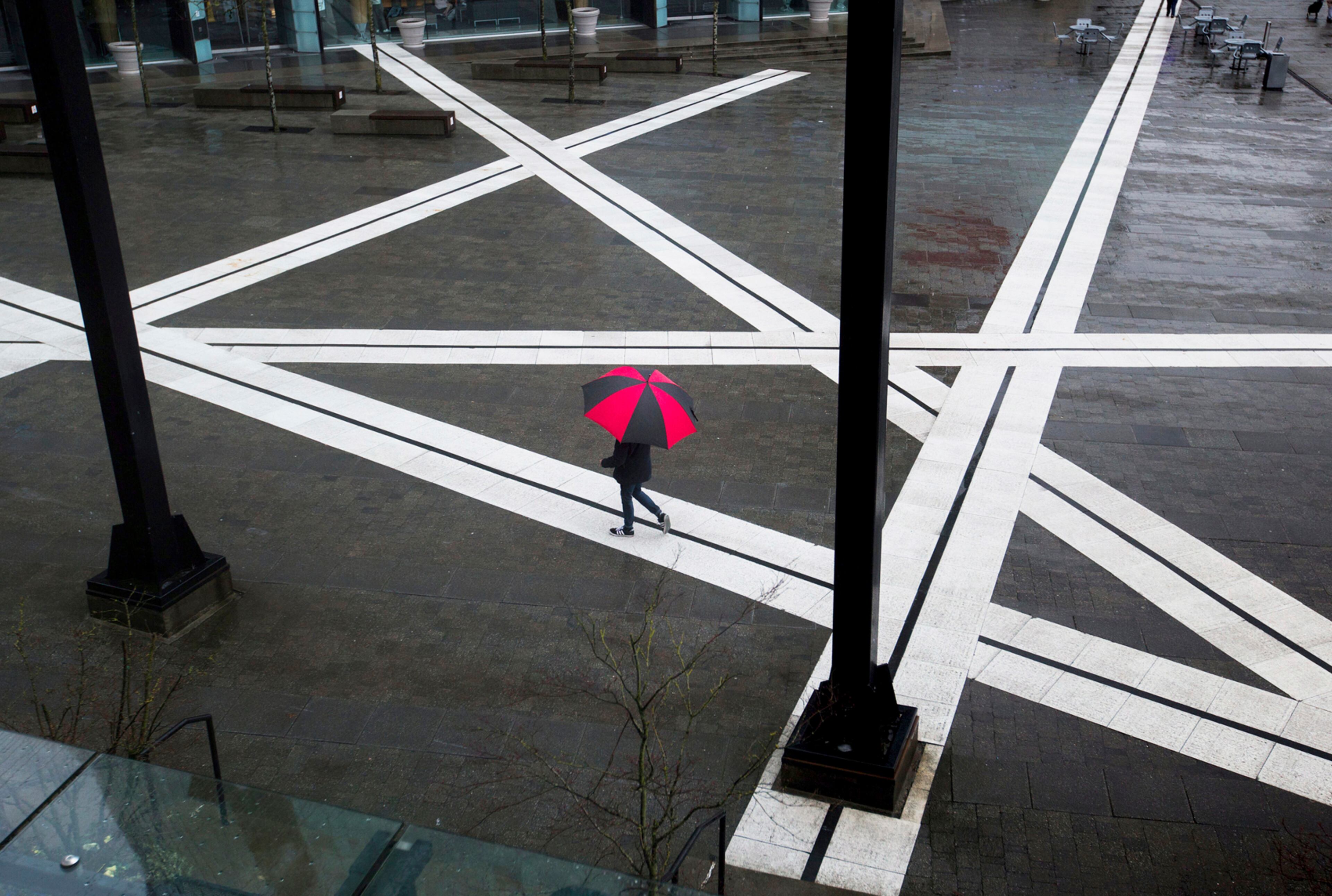 A pedestrian carrying an umbrella walks across the plaza at Central City as rain falls in Surrey, B.C., on Tuesday, March 28, 2017. (Darryl Dyck/The Canadian Press via AP)