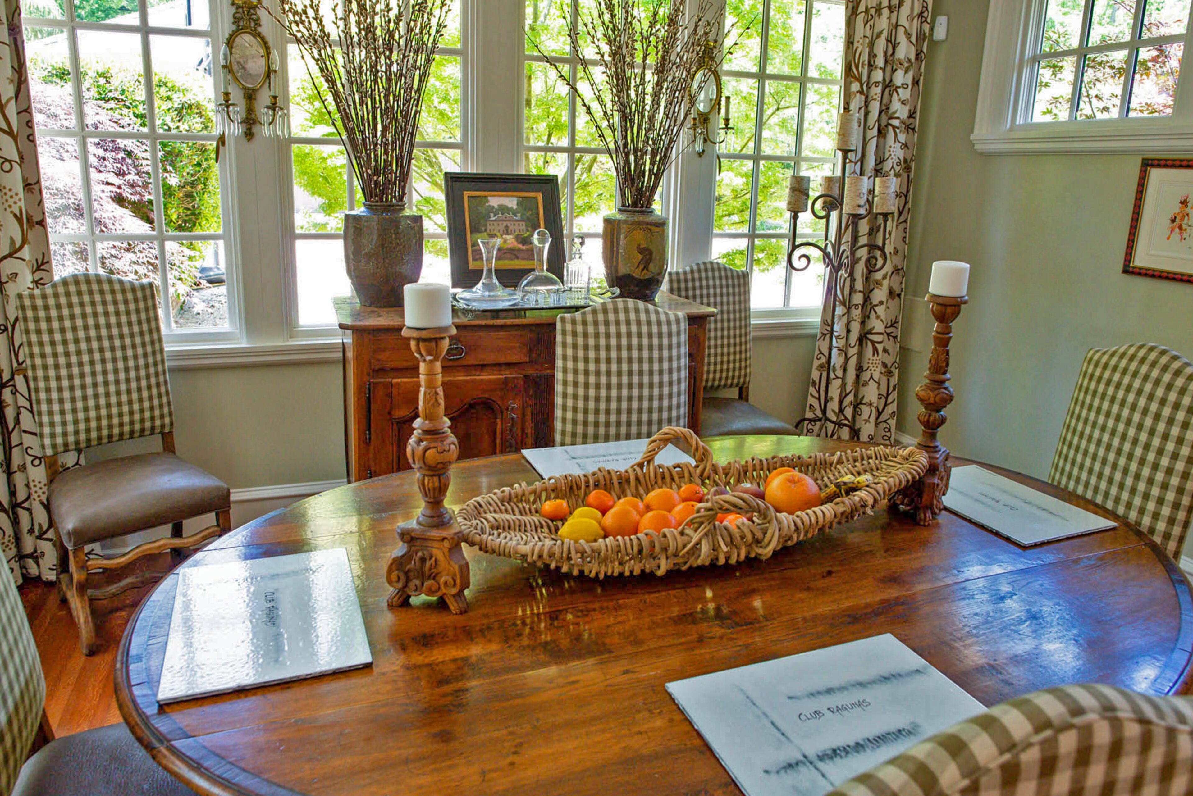 Dining chairs with gingham upholstery encircle a table in the eat-in kitchen. Crystals dangle from the sconces next to windows with views of the Japanese maples on the Druid Hills property.