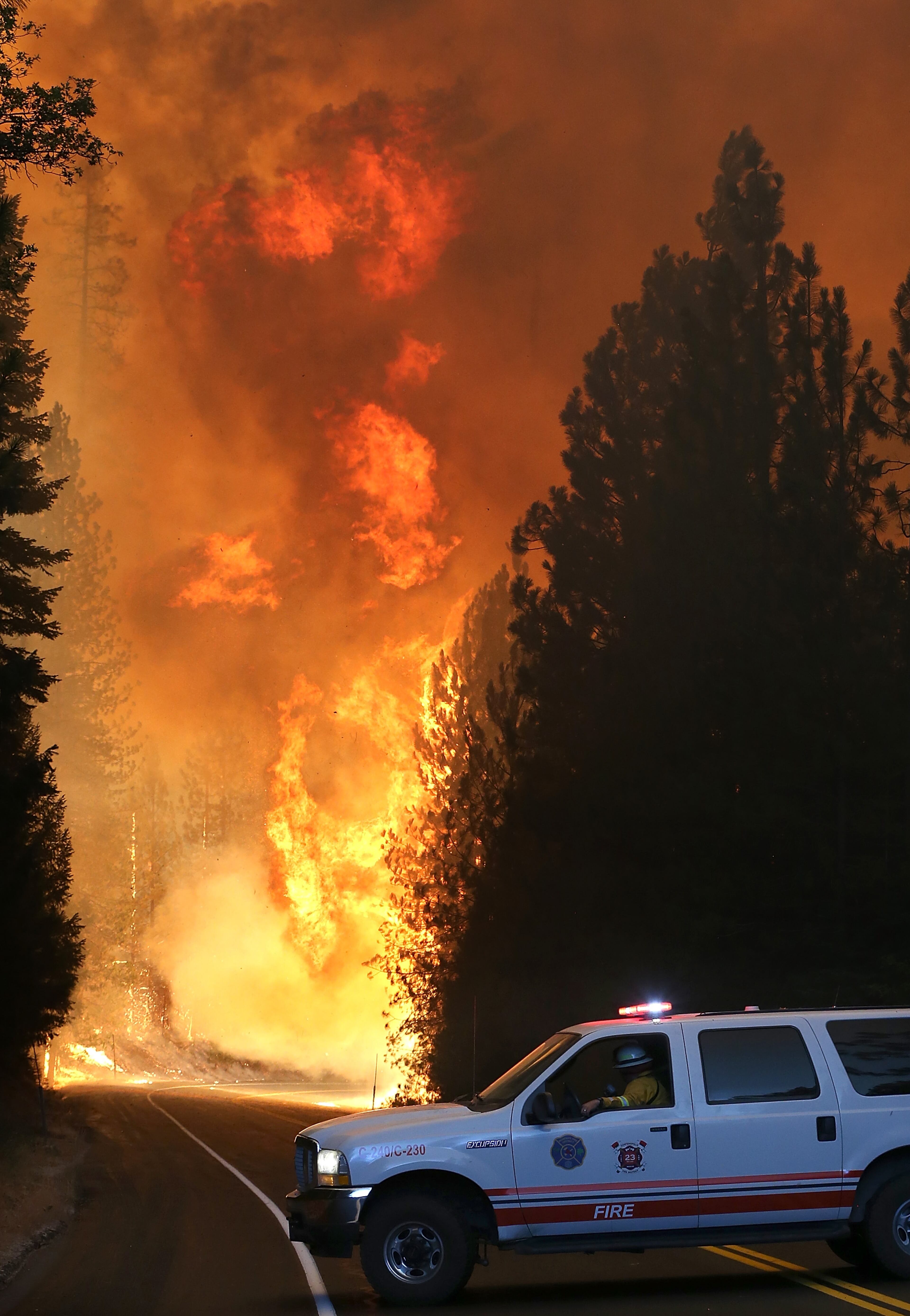 GROVELAND, CA - AUGUST 24: A Murphys Fire District firefighter stops his vehicle as a massive wall of fire from the Rim Fire consumes trees along highway 120 on August 24, 2013 near Groveland, California. The Rim Fire continues to burn out of control and threatens 4,500 homes outside of Yosemite National Park. Over 2,000 firefighters are battling the blaze that has entered a section of Yosemite National Park and is currently 5 percent contained. (Photo by Justin Sullivan/Getty Images)