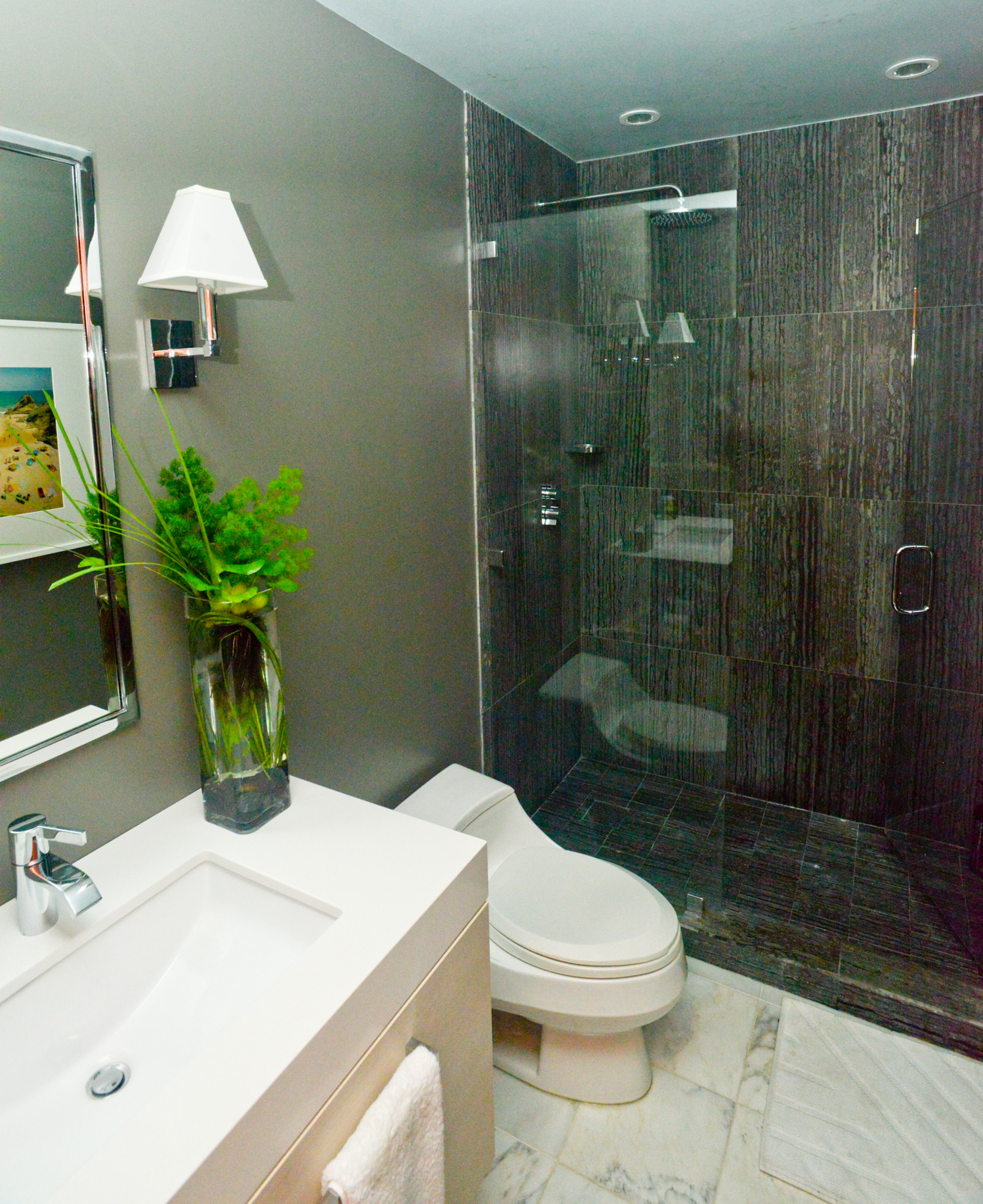 Homeowner Jason Moattar recently renovated his guest bathroom, gutting it and replacing the bathtub/shower combo with a glass shower made of sleek, charcoal tiles from Renaissance Tile & Bath. An aerial photograph of colorful umbrellas on a beach by Christian Chaize (reflected in the mirror) provides a pop of color.