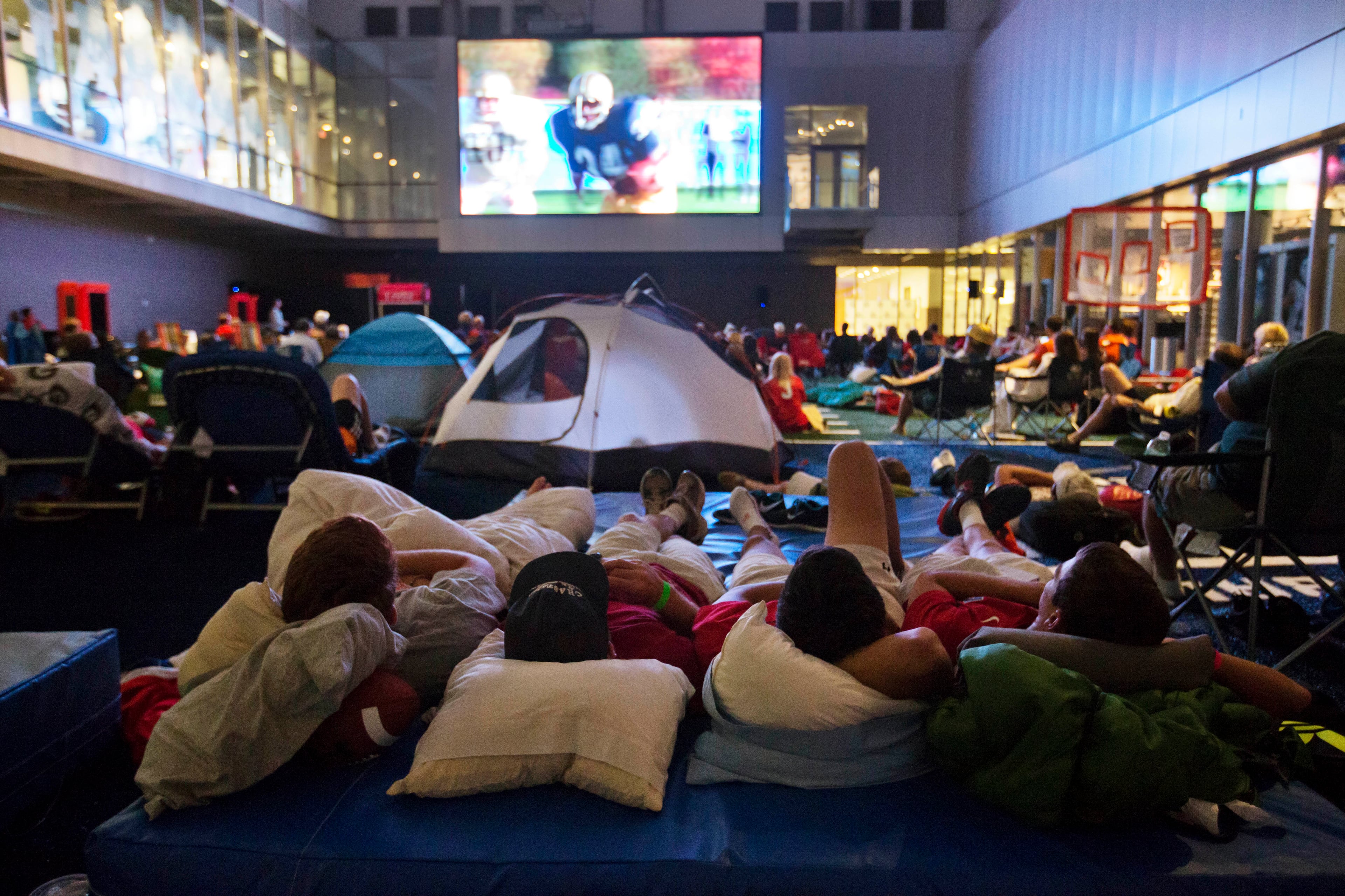 From left, Danny Mason, Walker Tuten, Nick Toomey and Matt Filer, watch the movie "Rudy" during a sleepover in the College Football Hall of Fame, Wednesday, Aug. 13, 2014, in Atlanta. The crowd fell asleep to the playing of college football themed movies such as "Rudy" and "We are Marshall" on the jumbotron. (AP Photo/David Goldman)