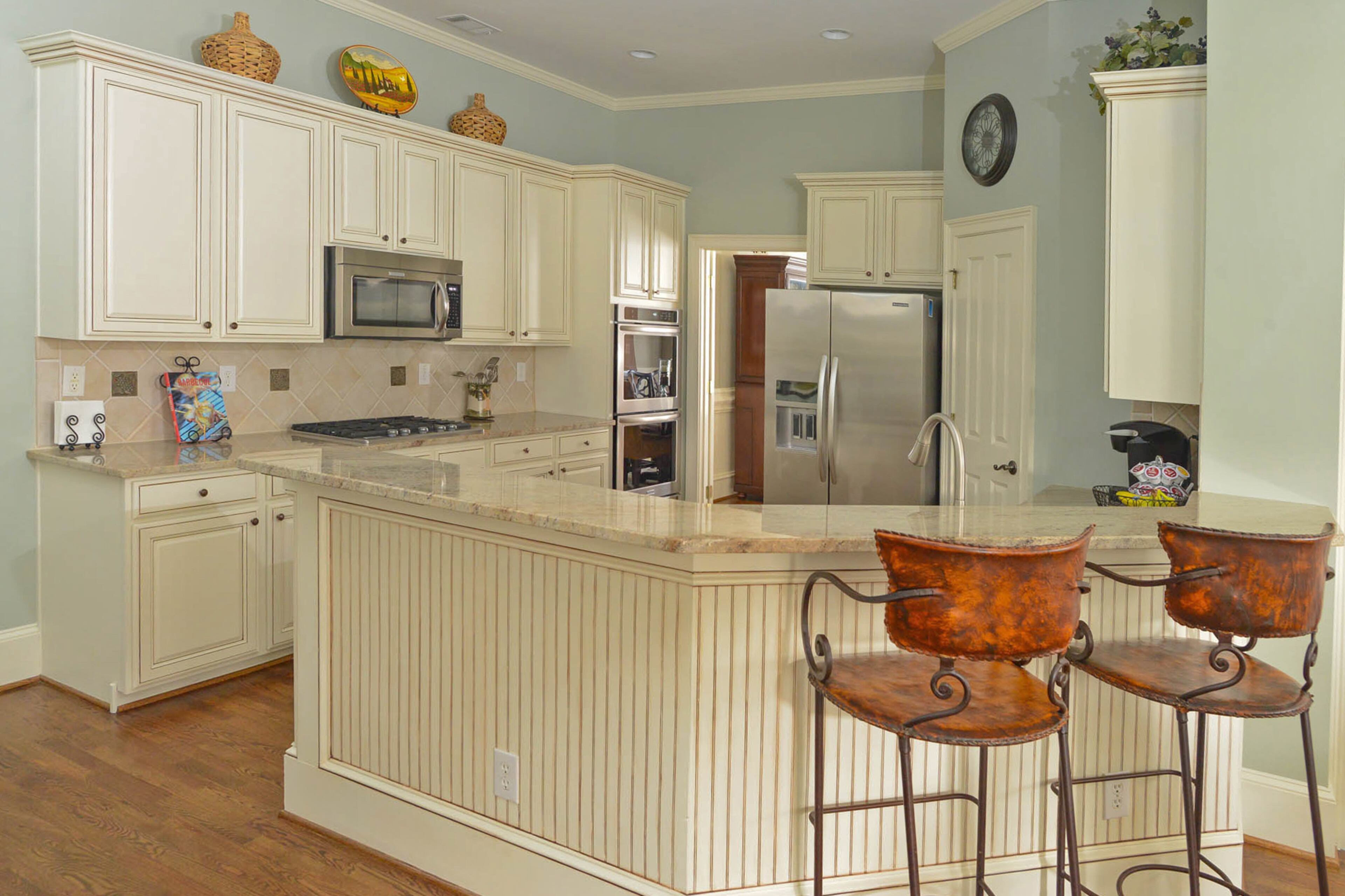 Euro Design installed new granite countertops in the kitchen, which has appliances from BrandsMart. After buying the home in 2013, Jim and Kathy Callahan also refinished the cabinets and installed new hardware as part of renovations by Mike Gatto of Vision Painting and Contractors. The wall's paint color is Sherwin-Williams Contented. A pair of leather bar stools from Arhaus pull up to the counter.