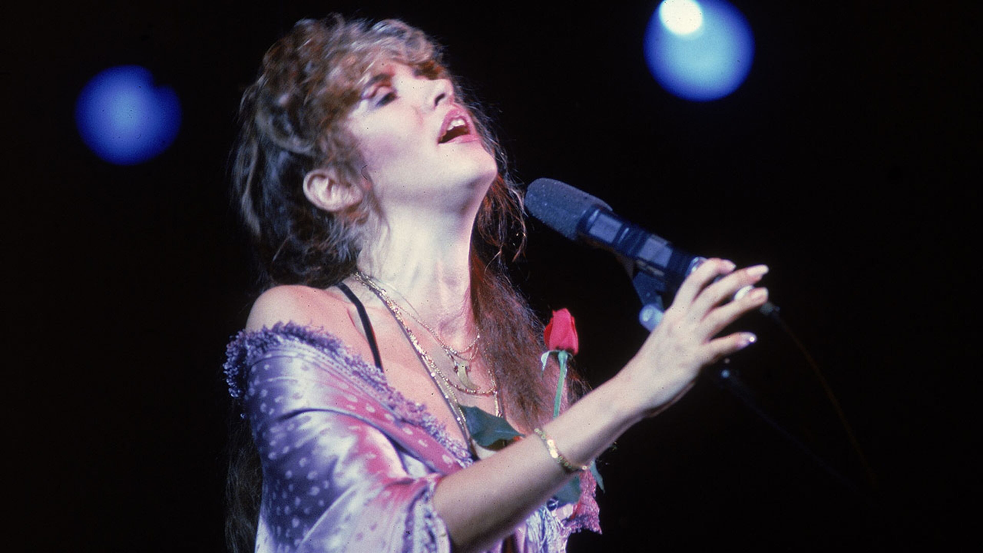 1992 - American pop and rock singer Stevie Nicks (of the group Fleetwood Mac) sings into a microphone onstage as she holds a rose against her chest, early 1990s. (Photo by Hulton Archive/Getty Images)
