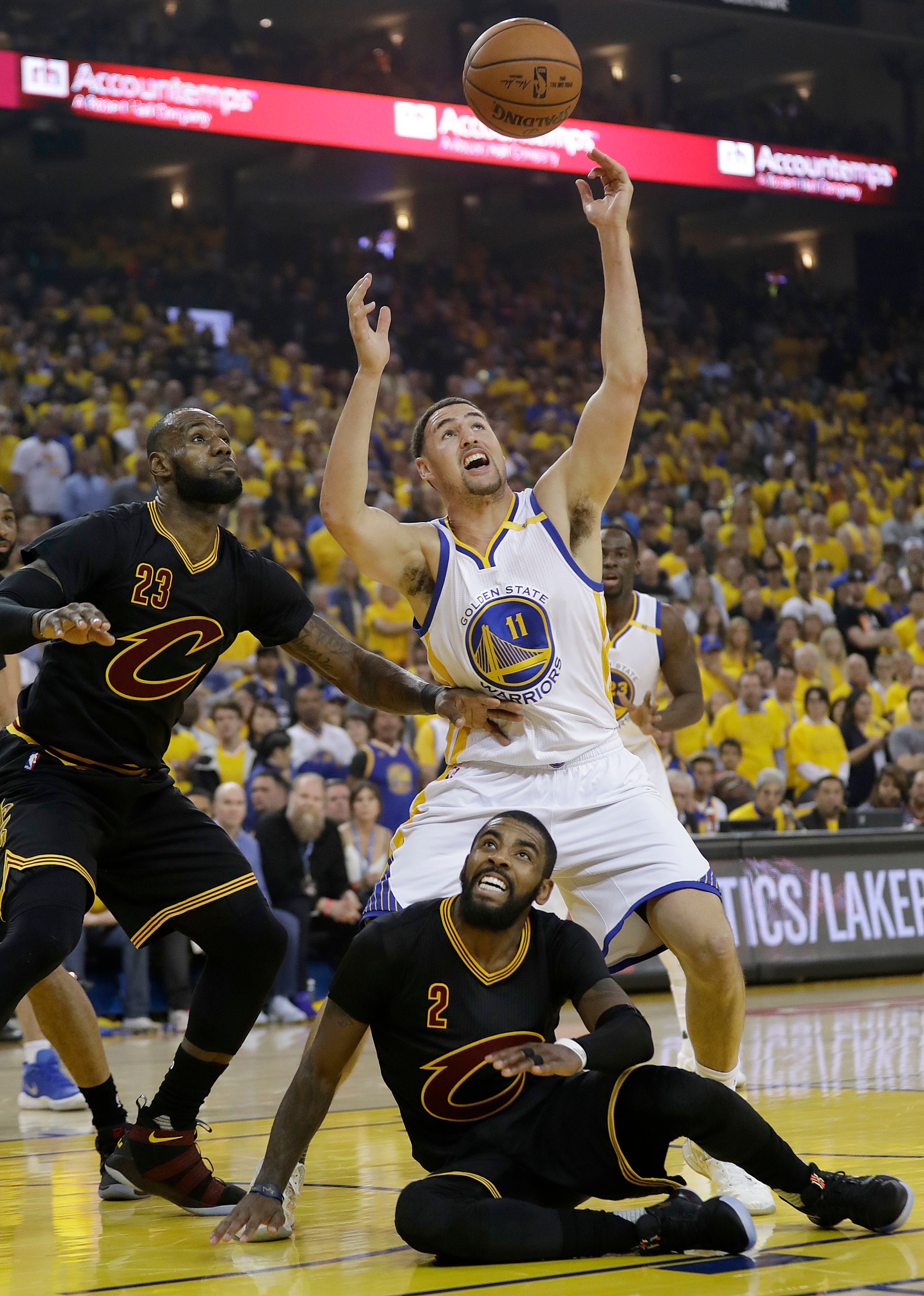Golden State Warriors guard Klay Thompson (11) reaches for the ball over Cleveland Cavaliers forward LeBron James (23) and guard Kyrie Irving (2) during the first half of Game 5 of basketball's NBA Finals in Oakland, Calif., Monday, June 12, 2017. (AP Photo/Marcio Jose Sanchez)