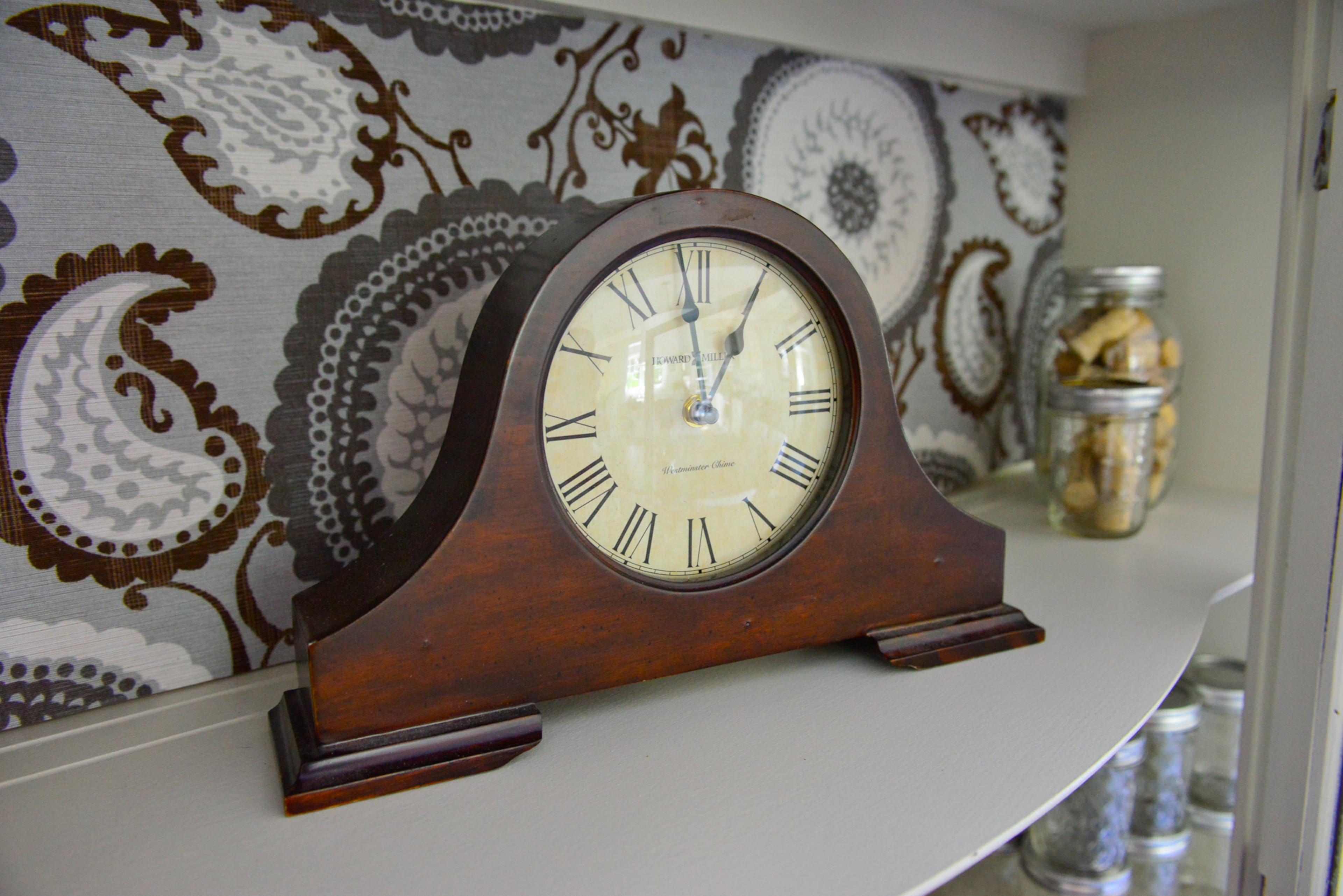 The homeowners repainted and distressed a china cabinet that once belonged to Heather Johnson's grandmother, then was passed down to her mother and then to her. A patterned tablecloth is re-purposed as the backing for the cabinet, to give it depth. Items on display include gifts such as a clock.