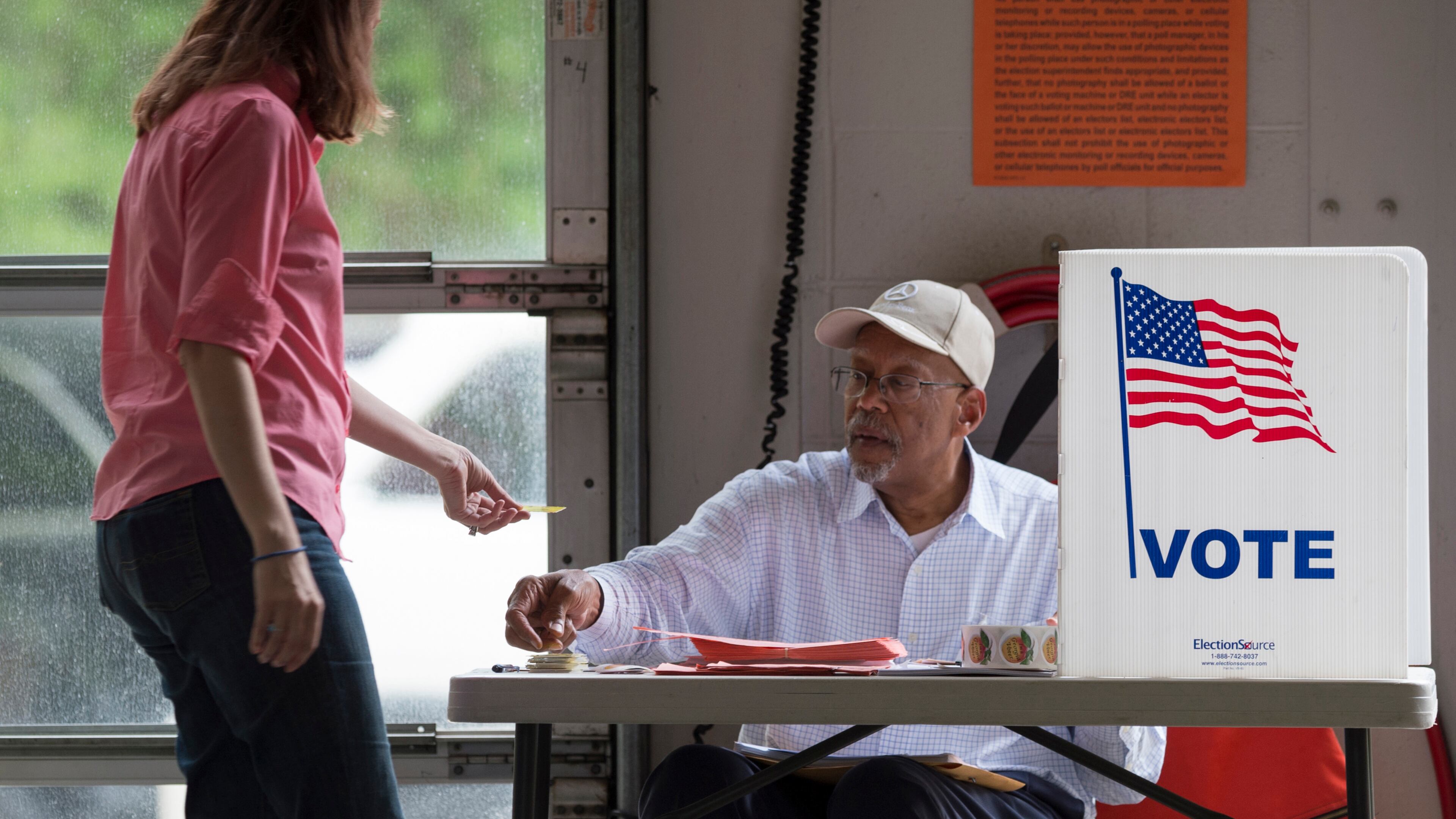 April 18, 2017, Alpharetta - Alpharetta resident Toni Kuhn, left, hands her voter card to Birdel Jackson III, center, at Alpharetta Fire Station 82 in Alpharetta, Georgia, on Tuesday, April 18, 2017. Cobb, Fulton and North DeKalb residents cast ballots today for the highly contested 6th Congressional District race. (DAVID BARNES / DAVID.BARNES@AJC.COM)
