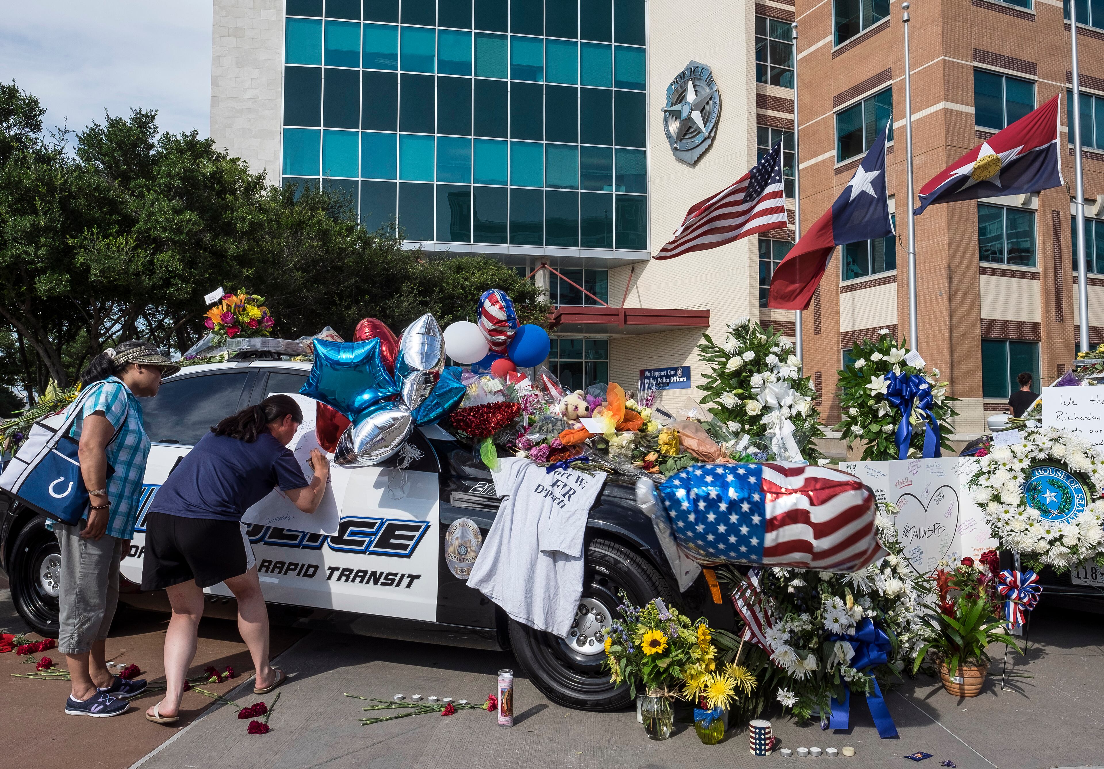 July 8, 2016 - Carolyn Tillett, right, rights on a card as her mother, Azucena Tillett, left, looks on as they pay their respects at a memorial of flowers, gifts and cards placed on Dallas patrol cars in front of the Dallas Police department headquarters in Dallas, Texas, on Friday, July 8, 2016. Five officers were killed, six officers wounded along with two civilians were shot by suspected sniper Micah Johnson. RODOLFO GONZALEZ / AUSTIN AMERICAN-STATESMAN