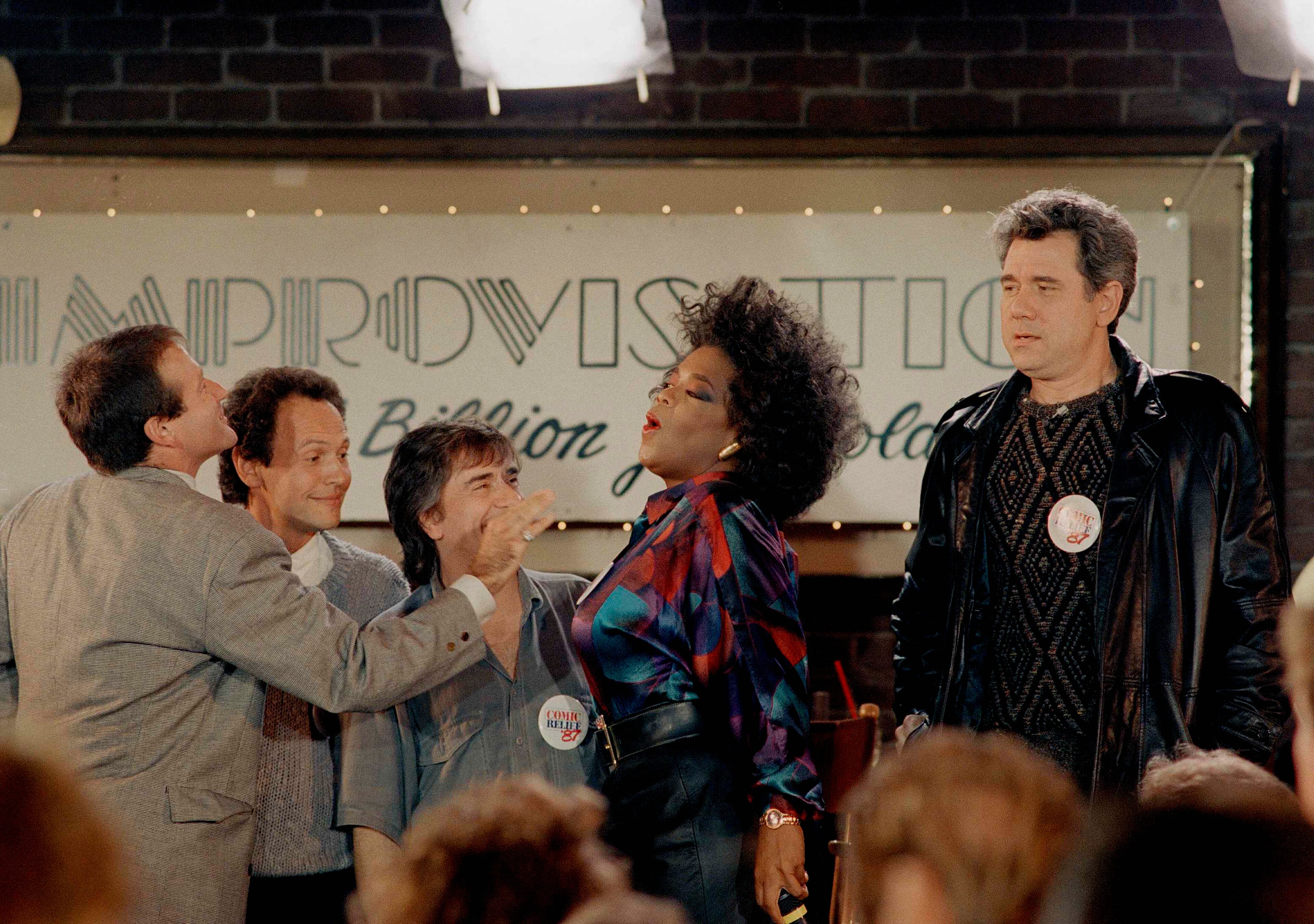 Comedian Robin Williams, left, reaches out as if to touch talk show host Oprah Winfrey, right, after taping of her show, "The Oprah Winfrey Show," at the Improvisation in Los Angeles, Calif., Nov. 8, 1987. Looking on are comedians Billy Crystal, second from left, and Dudley Moore. The show which will air, Nov. 12 examines the upcoming "Comic Relief" benefit comedy show which will air November 14 on HBO. (AP Photo/Lennox McLendon)