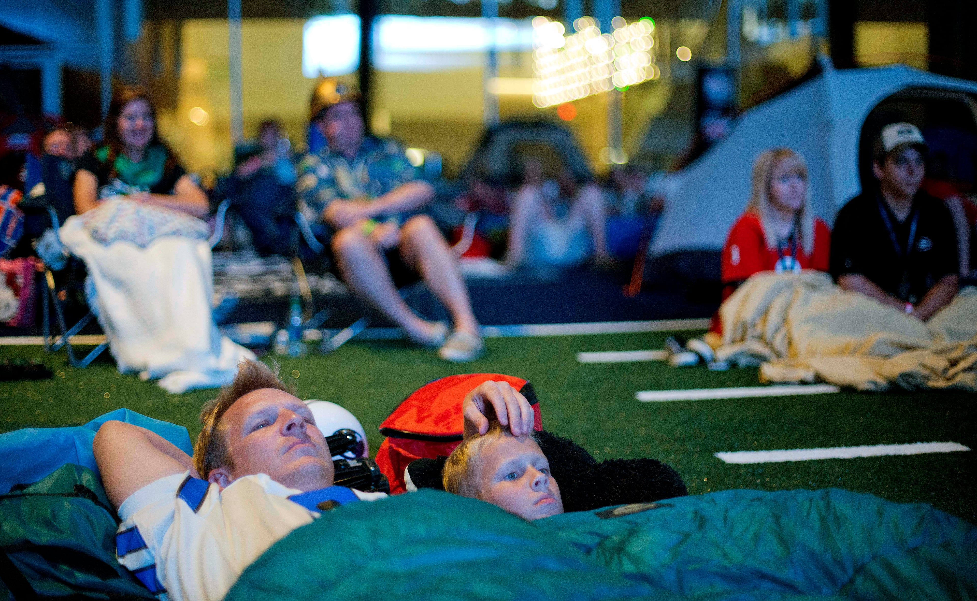 Chip Kent and his son C.J., 9, of Suwanee, Ga., watch from their sleeping bags as the movie "Rudy" is played during a sleepover in the College Football Hall of Fame just after midnight, Thursday, Aug. 14, 2014, in Atlanta. One hundred contest winners who had to write an essay detailing their love of college football were selected to stay with a guest overnight in Atlanta's College Football Hall of Fame before its grand opening and win a year's supply of Chick-fil-A. The crowd of 200 who came from as far away as Hawaii were among the first to experience the College Football Hall of Fame and Chick-fil-A Fan experience before it opens to the public on Aug. 23. After touring the exhibits guest were served dinner on the football field before pitching their tents on the turf and settling in for the night as college football themed movies such as "Rudy" were played on the jumbotron. The hall was previously located in South Bend, Indiana, but was plagued by poor attendance. (AP Photo/David Goldman)