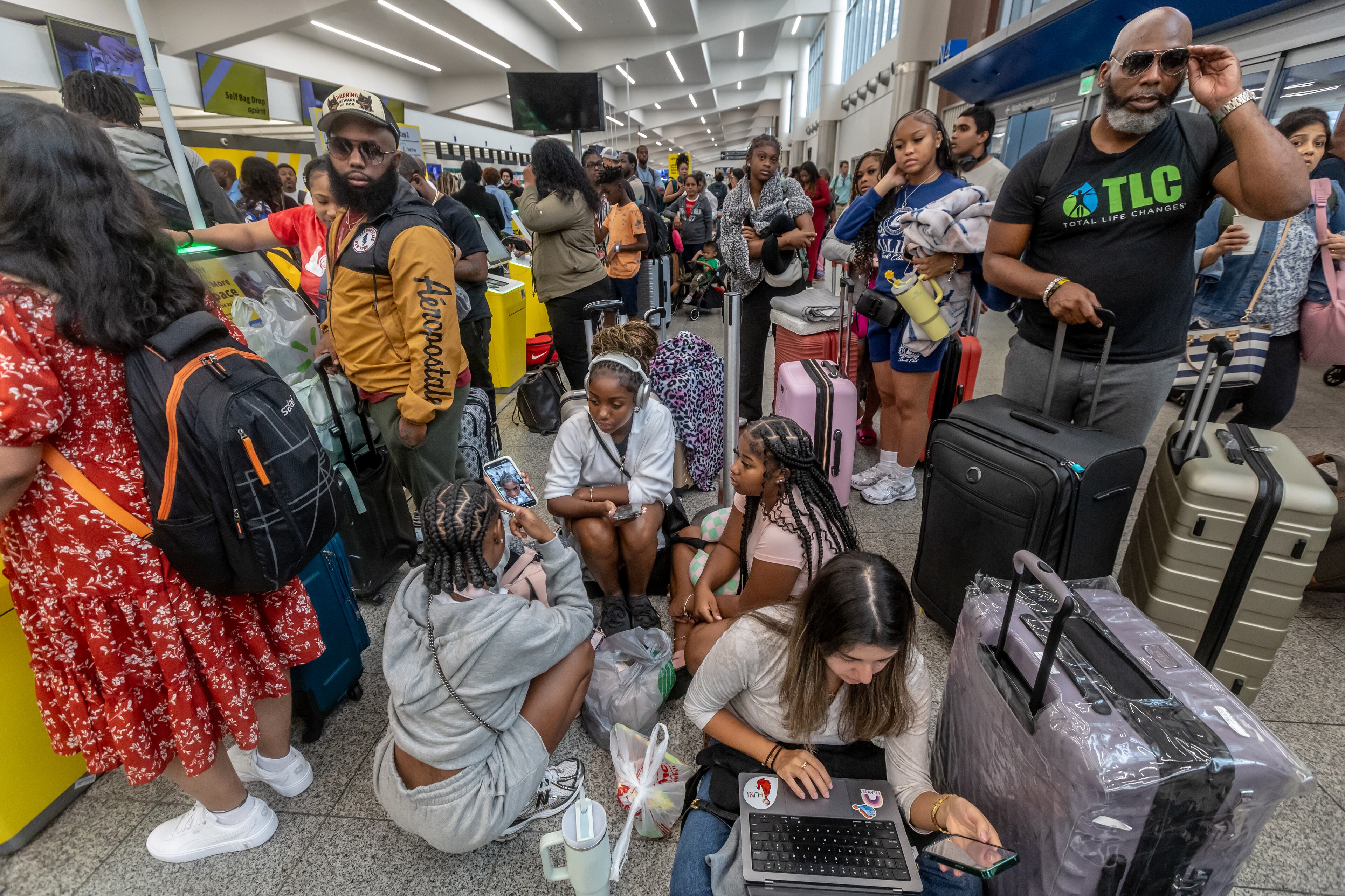 Torry Wallace (right) waits with his stepdaughter’s friends and family in the North Terminal last year after a computer outage canceled thousands of flights.. (John Spink/AJC 2024)
