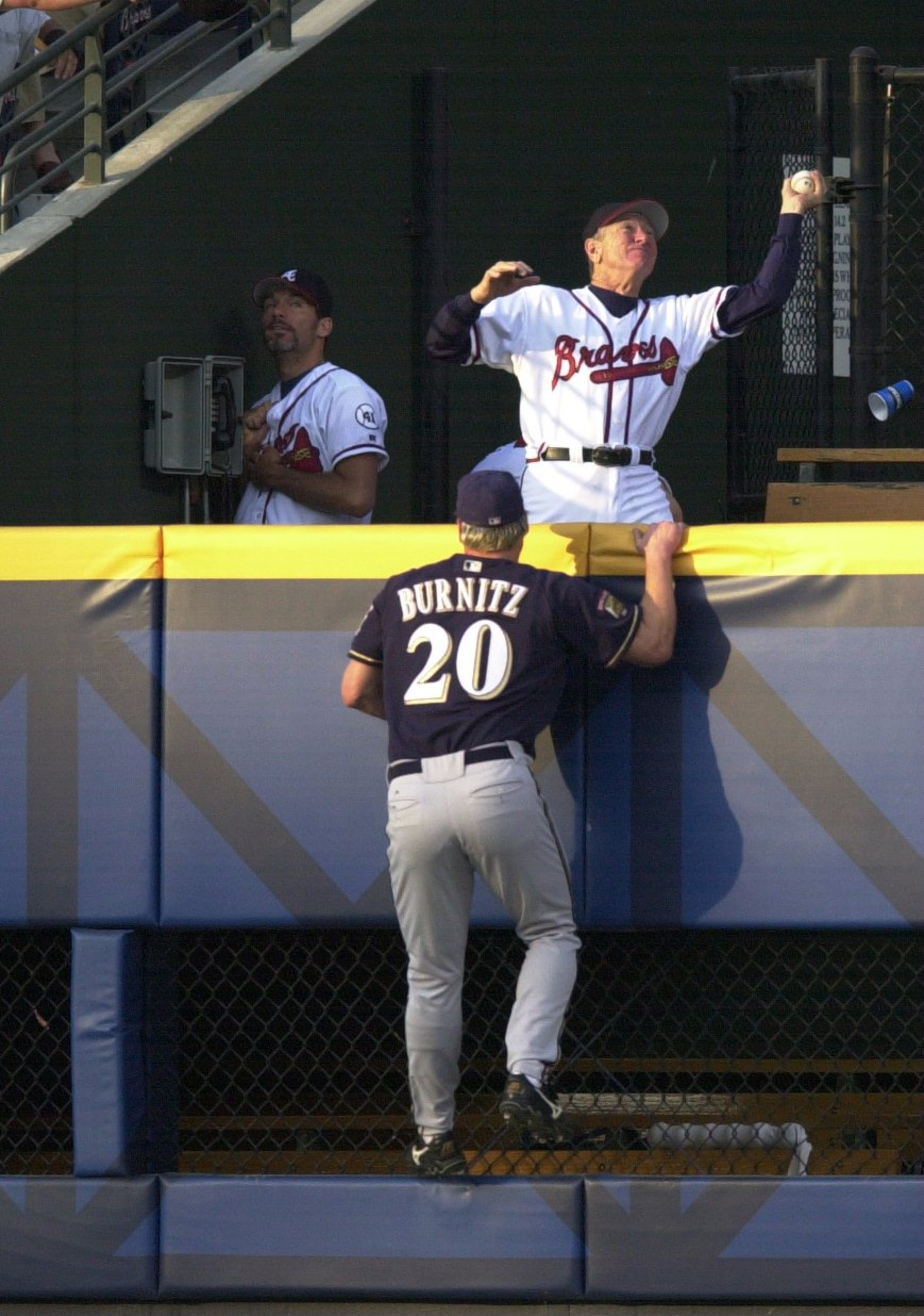 010417 Atlanta, GA: Braves bullpen coach Bobby Dews catches B.J. Surhoff's solo homerun that was hit in the 2nd inning as Brewers Jeromy Burnitz climbs up to the Braves bullpen to try and get it, running out of the way in the bullpen was Mike Remlinger, left against the Milwaukee Brewers. STAFF PHOTO BY: MARLENE KARAS