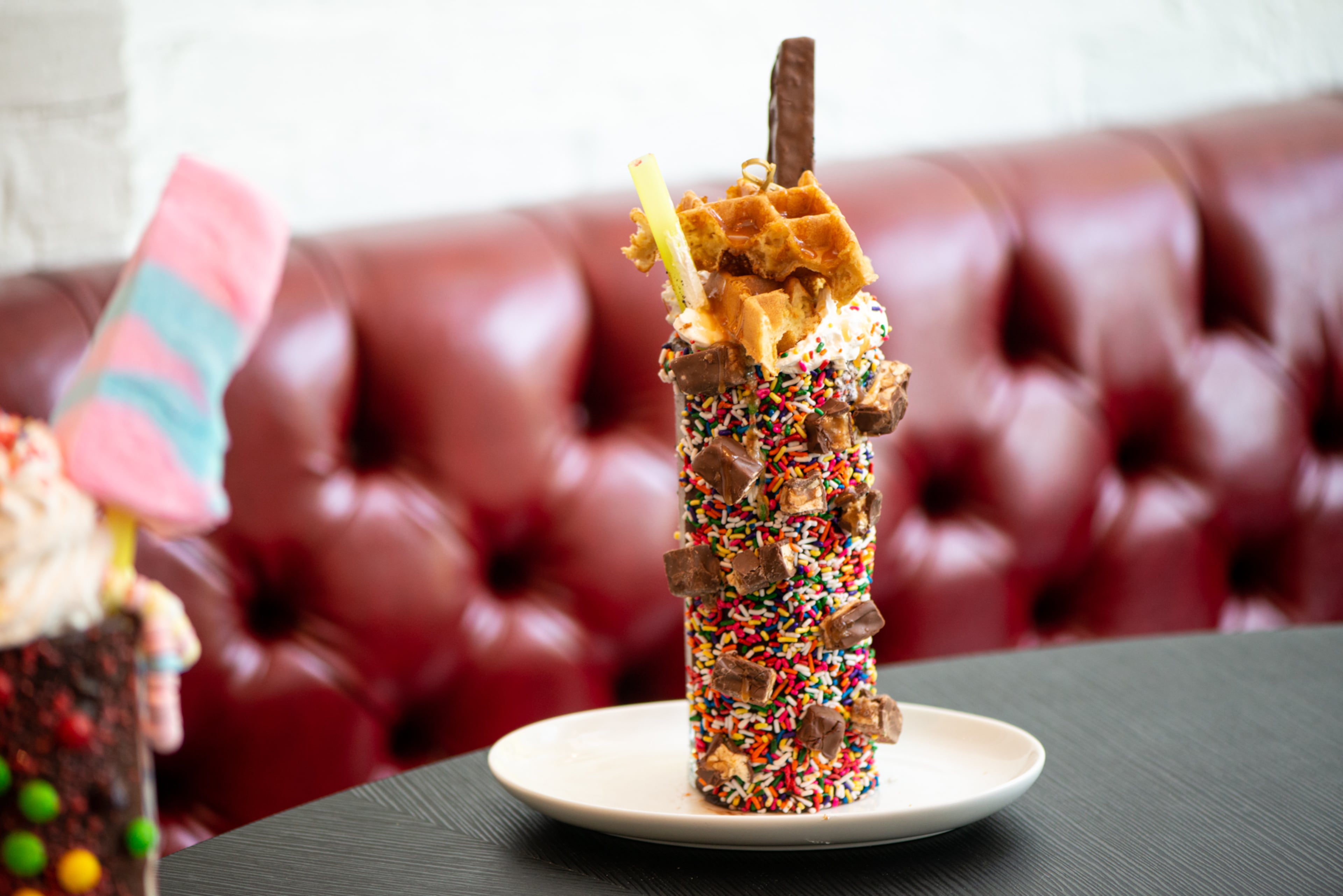 The Sugar Factory Giggles Snickers Milkshake, cookies and cream ice cream blended with toasted peanuts, topped with a caramel waffle, snickers, whipped cream, and sprinkles served in a chocolate covered mug with Snickers pieces and rainbow sprinkles.