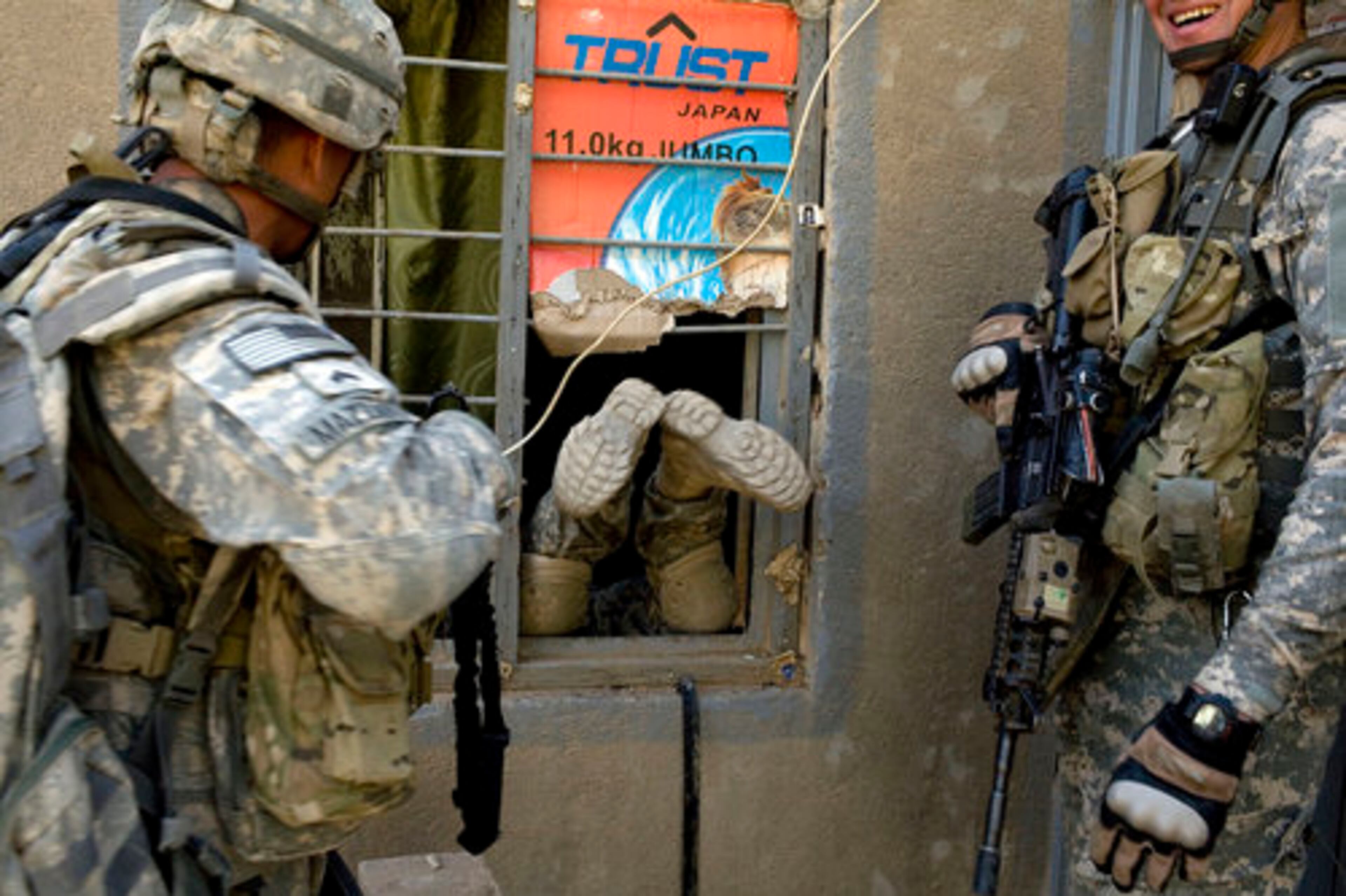 Soldiers with the U.S. Army's 1st Platoon, Charlie Company, 1/21 laugh as a colleague slips into an empty building through a small window during a search for weapons in the village of Fira Shiha, near Abu Ghraib, on Wednesday.