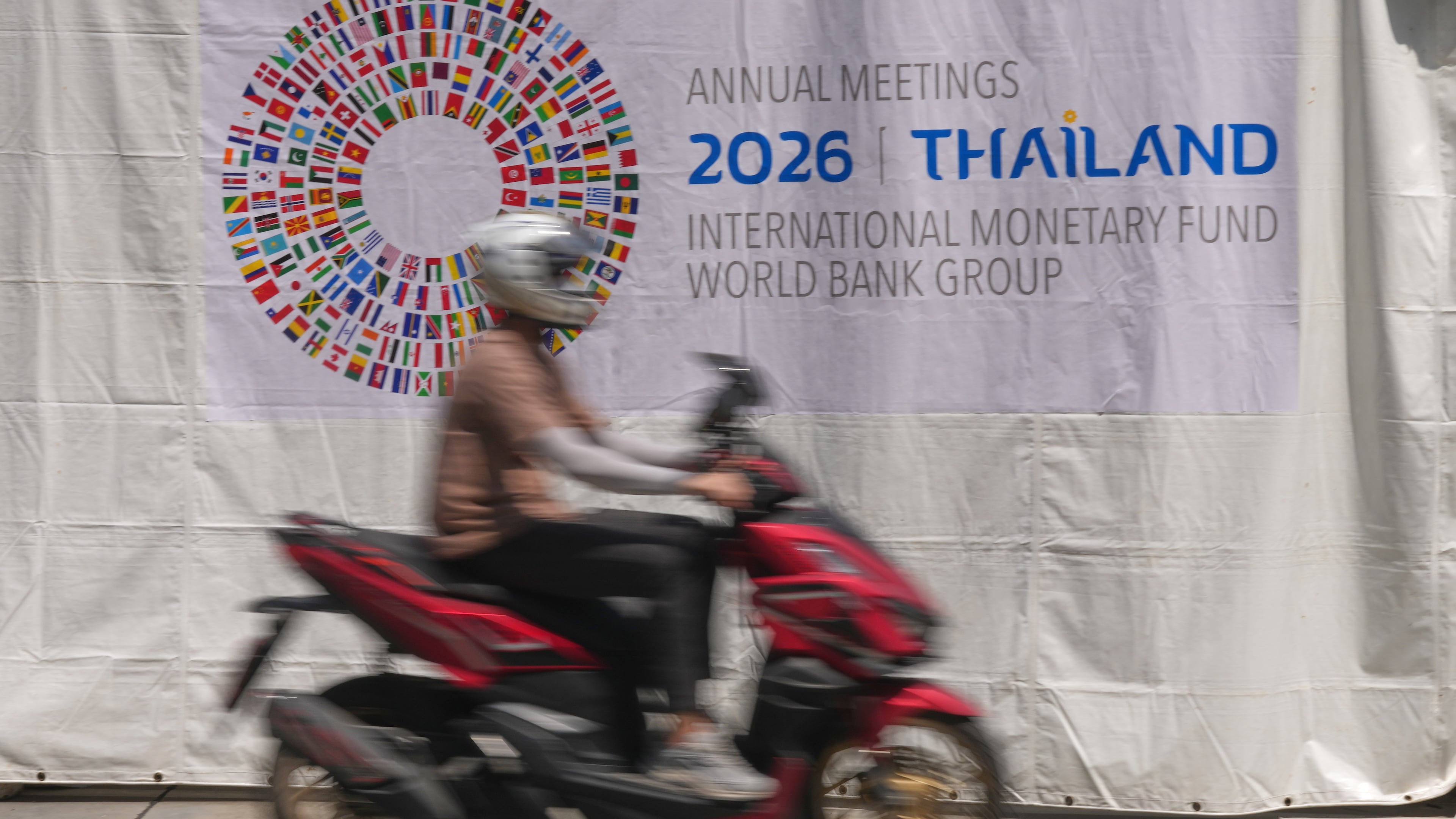 A motorcycle taxi rides past a banner at the Queen Sirikit National Convention Center ahead of the annual meetings of the International Monetary Fund (IMF) and the World Bank Group in Bangkok, Thailand, Friday, Oct. 9, 2026. (AP Photo/Sakchai Lalit)