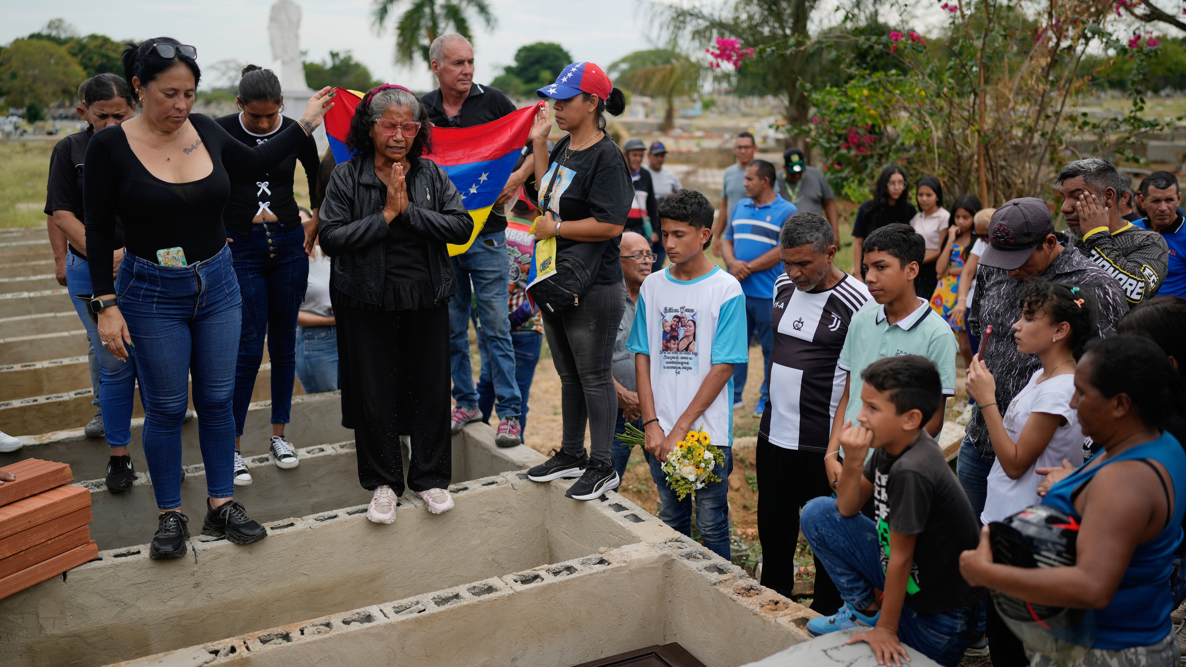 Relatives of Edilson Torres, a Venezuelan police officer who died in prison a month after being arrested on accusations of treason, gather around his grave during his funeral in Guanare, Venezuela, Tuesday, Jan. 13, 2026. (AP Photo/Ariana Cubillos)