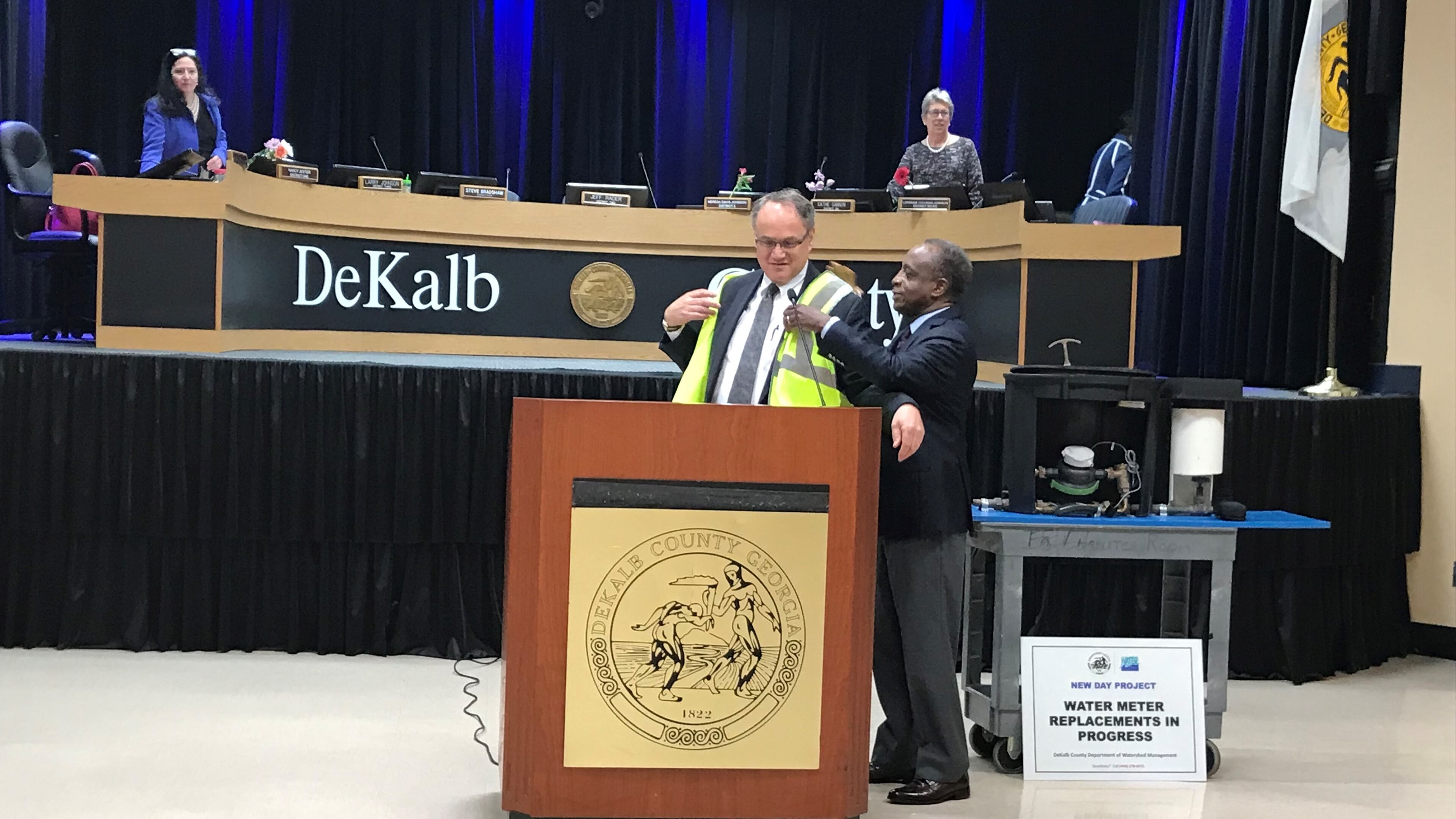 DeKalb County CEO Michael Thurmond (right) puts a DeKalb New Day Project work vest on Jeff Rader, presiding officer of the county commission after a presentation on the initiative during the meeting on March 12, 2019. (TIA MITCHELL/TIA.MITCHELL@AJC.COM)