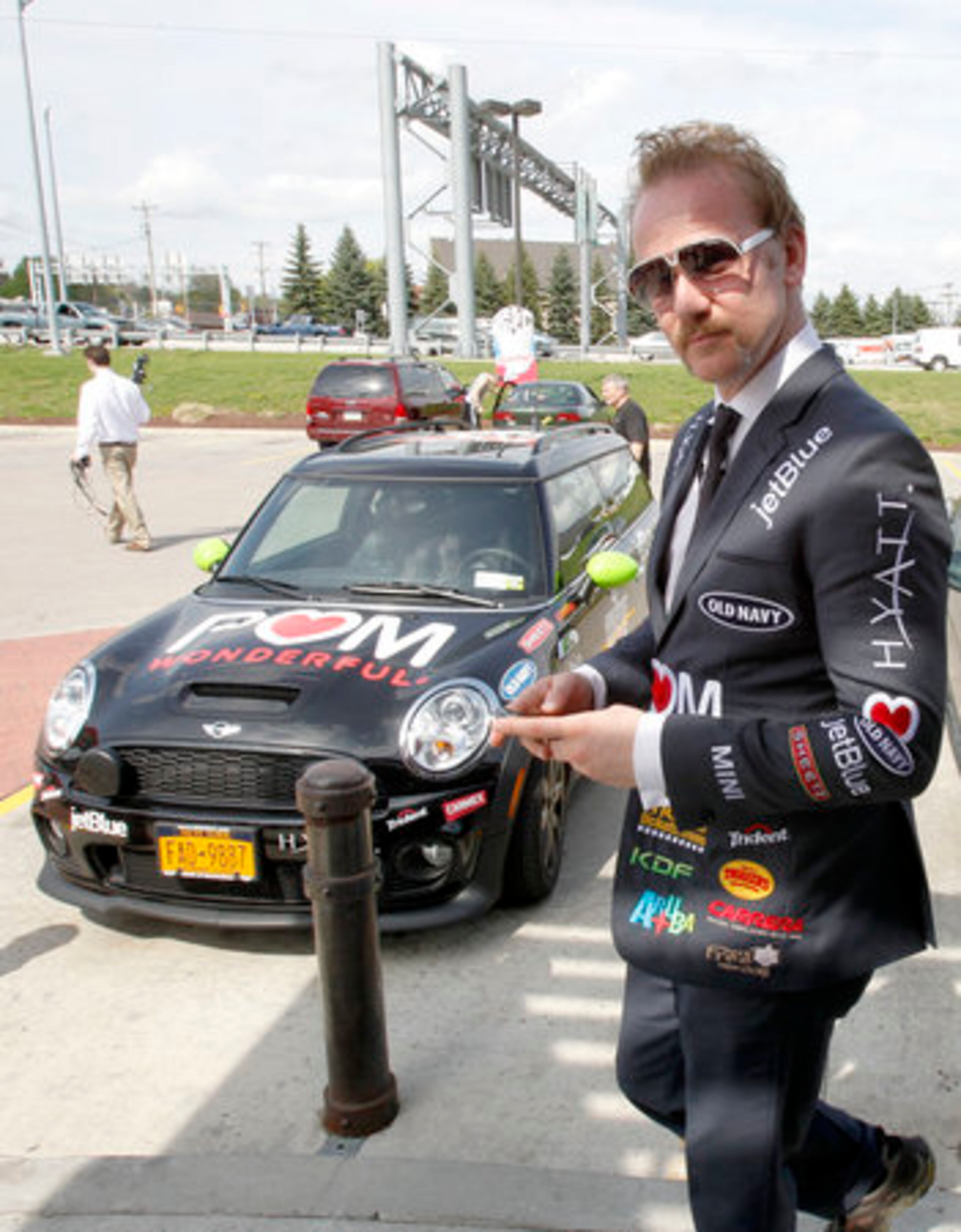 Spurlock, wearing a suit with sponsors names stitched onto it, walks by a Mini Cooper, one of the sponsors in his recent movie, as he leaves a Sheetz convenience store after a promotional stop