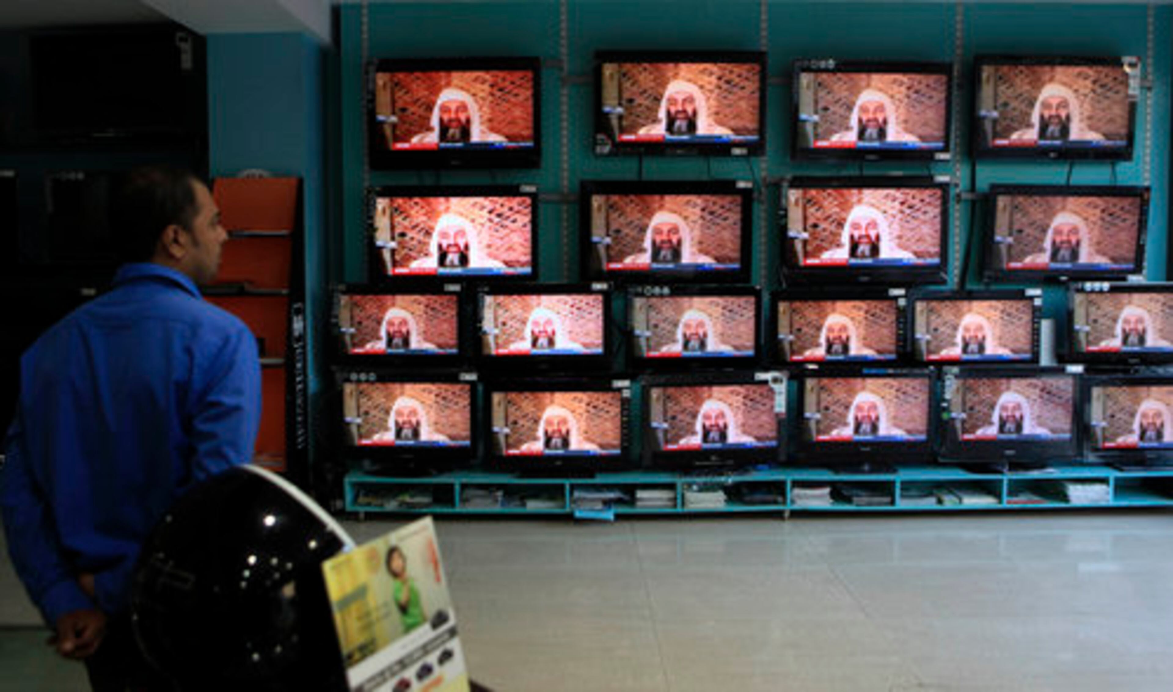 A sales person stands in his shop as a TV news reports the killing of Osama bin Laden in Mumbai, India, Monday, May 2, 2011.