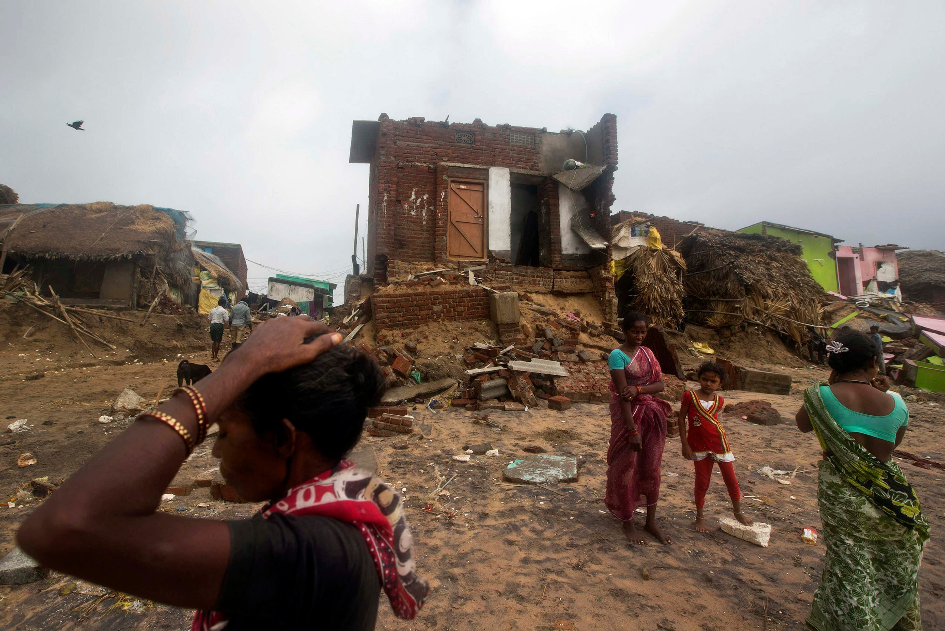 Fisherwomen and a girl stand in front of damaged house after Cyclone Phailin hit Puri in the eastern Indian state of Odisha October 14, 2013. A mass evacuation saved thousands of people from India's fiercest cyclone in 14 years, but aid workers warned a million would need help after their homes and livelihoods were destroyed. Cyclone Phailin was expected to dissipate within 36 hours, losing momentum on Sunday as it headed inland after making landfall from the Bay of Bengal, bringing winds of more than 200 kph (125 mph) that ripped apart tens of thousands of thatched huts, mangled power lines and tore down trees. REUTERS/Ahmad Masood