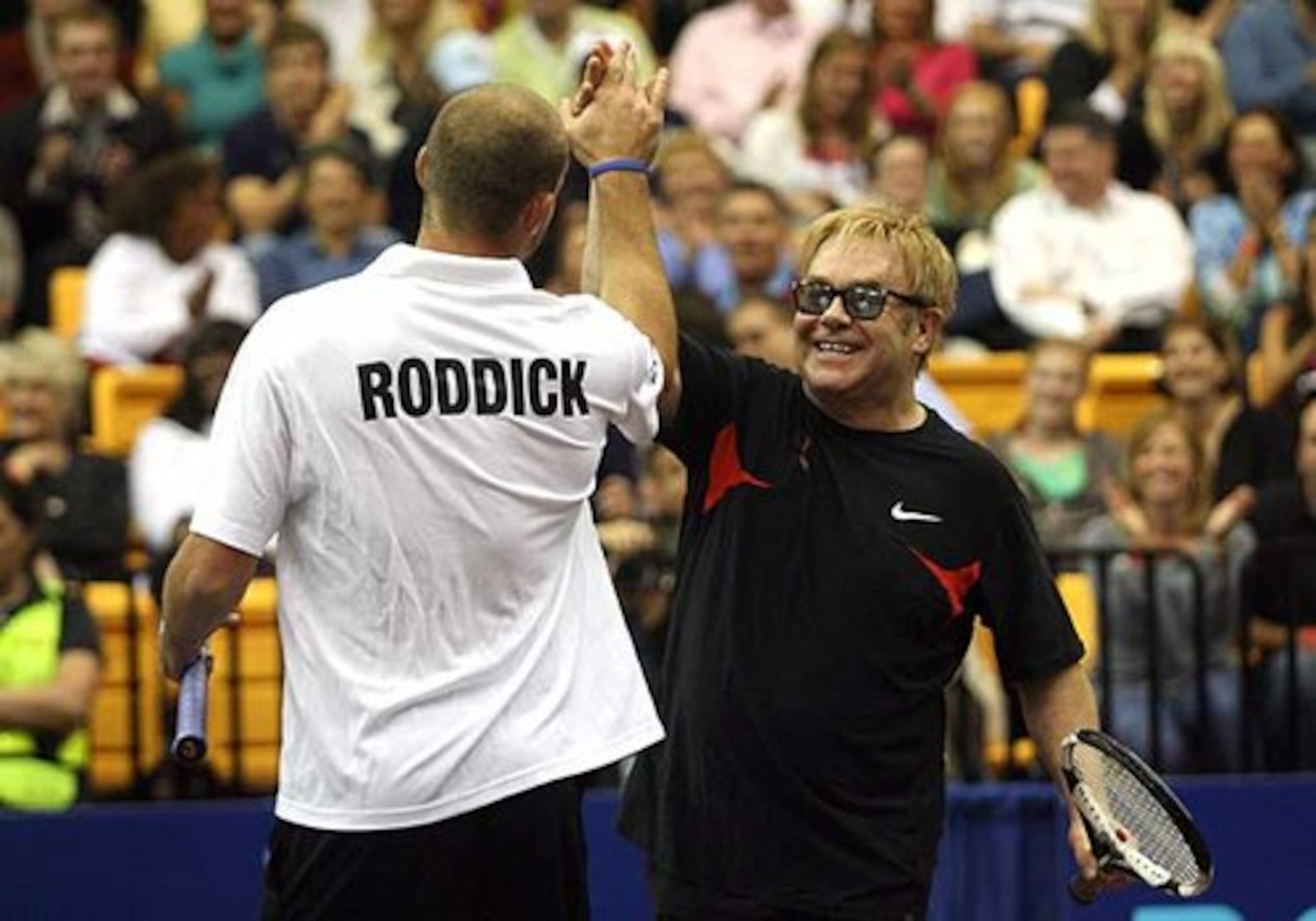 Andy Roddick and Elton John celebrate winning a point during a doubles match at the Advanta WTT Smash Hits tennis event.