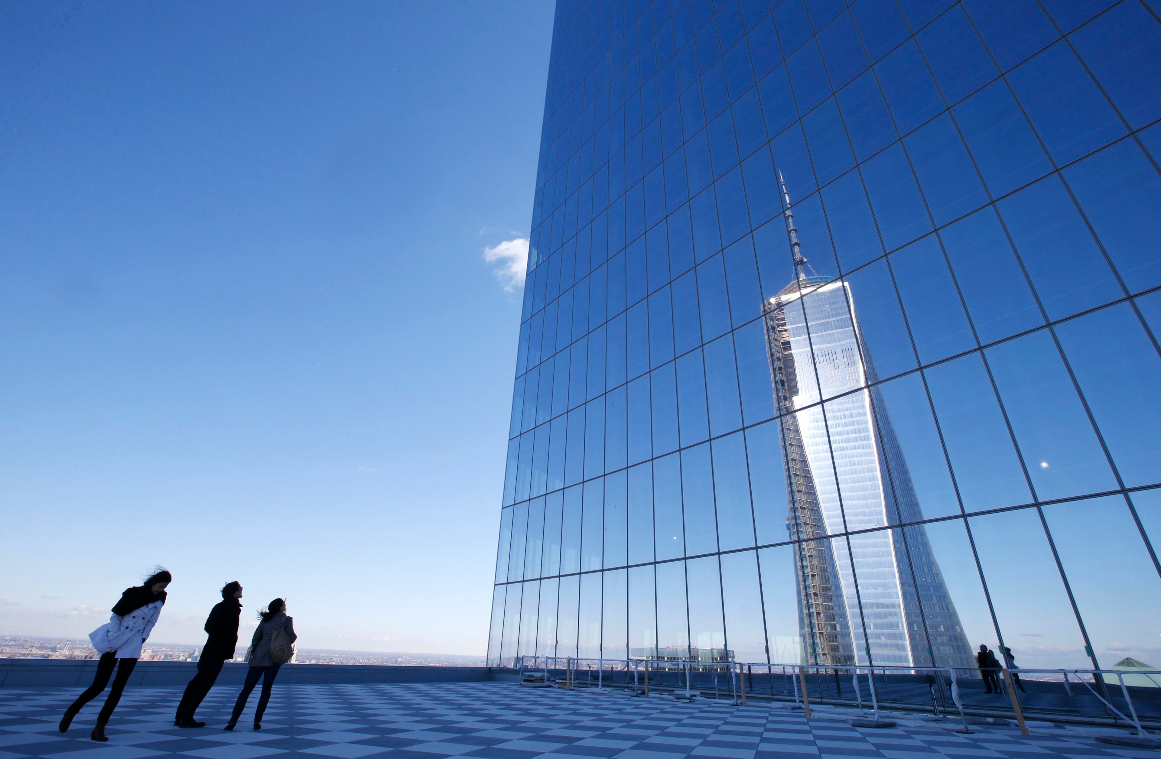 People on a press tour look up at a reflection of the One World Trade Center tower from a terrace on the 57th floor of the soon to be opened 4 World Trade Center tower in New York, November 8, 2013. 4 World Trade center sits at the south east corner of the World Trade Center site and will be the second tower to open on the site since the 2001 attacks on the World Trade Center. REUTERS/Mike Segar (UNITED STATES - Tags: BUSINESS CITYSCAPE)