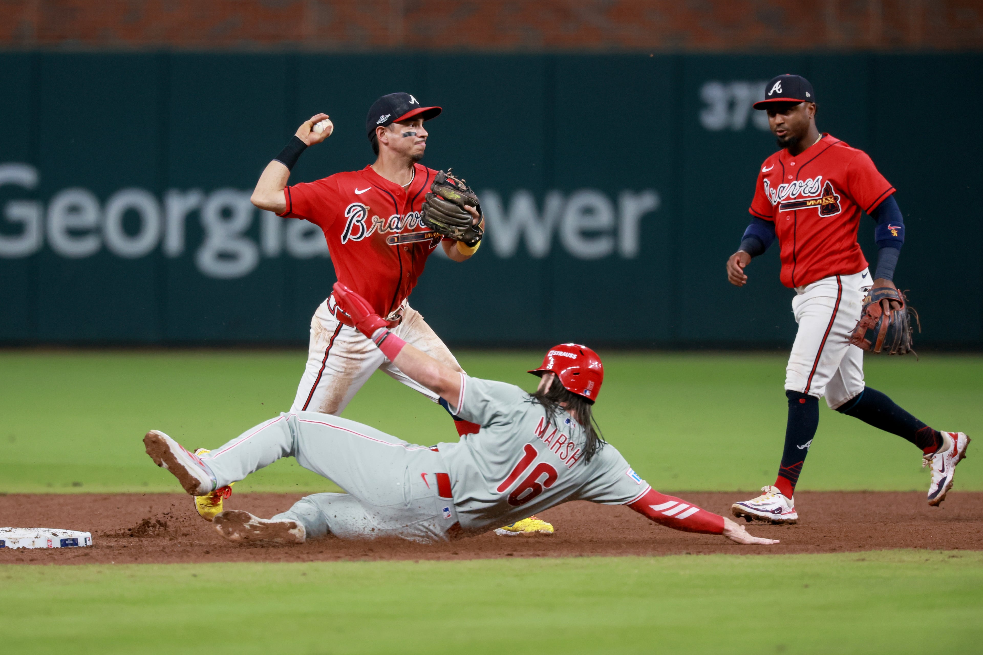 Braves left fielder Mauricio Dubón (left) turns an inning-ending double play against Phillies left fielder Brandon Marsh as Braves second baseman Ozzie Albies looks on during Game 3 of their NL Wild Card Series on Thursday, Oct. 1, 2026, in Atlanta. (Jason Getz/AJC)