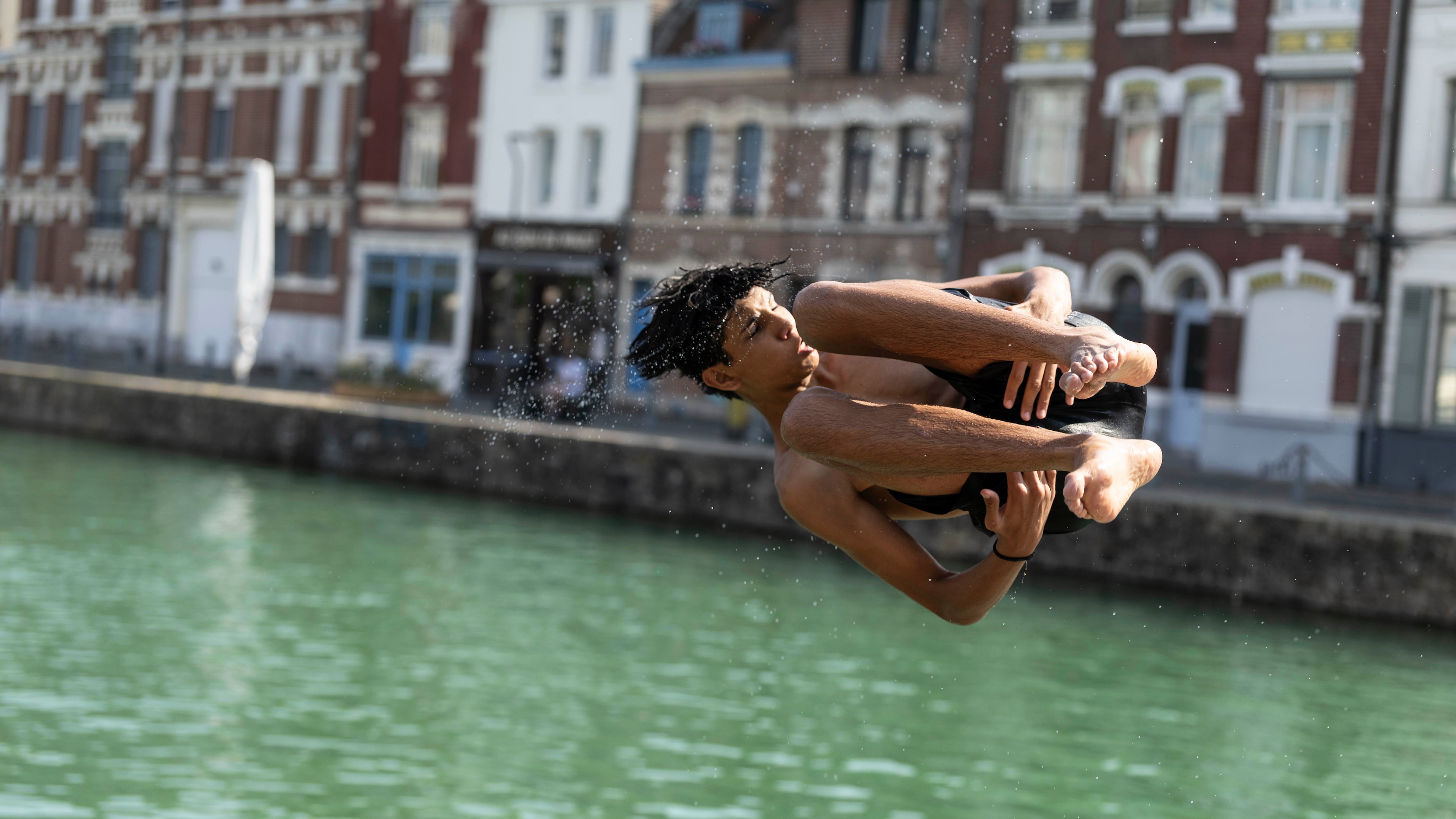 A young man dives into the water, in Lille, northern France, Monday June 22, 2026. (AP Photo/Jean-Francois Badias)