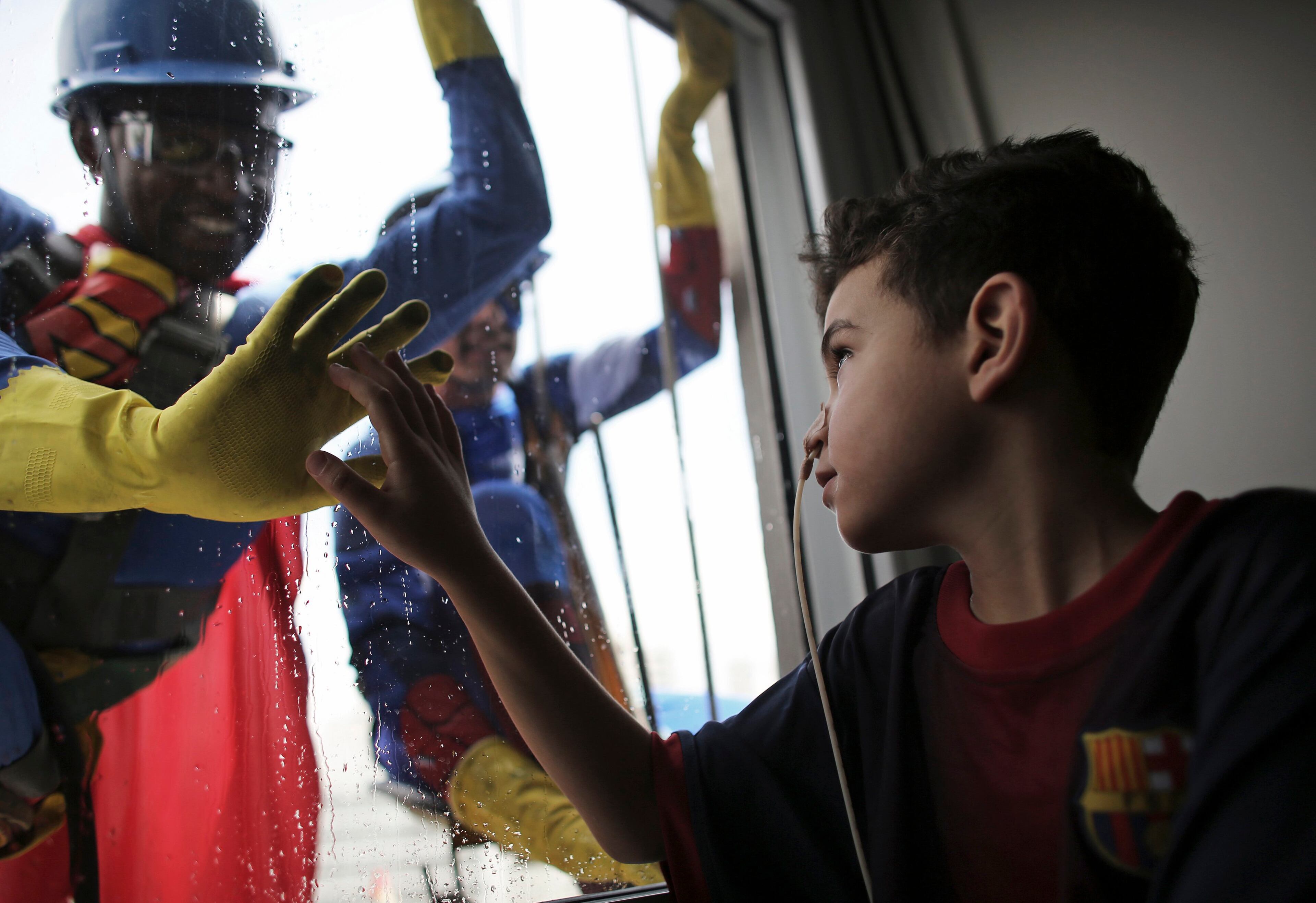 Men dressed as Superman (L) and Captain America smile at patient Caue Rodrigues Silvano, 7, wearing an FC Barcelona jersey, who looks on inside Hospital Infantil Sabara in Sao Paulo October 11, 2013. The costumed men cleaned the glass facade of the children's hospital, and met with patients. Brazil celebrates Children's Day on October 12. REUTERS/Nacho Doce