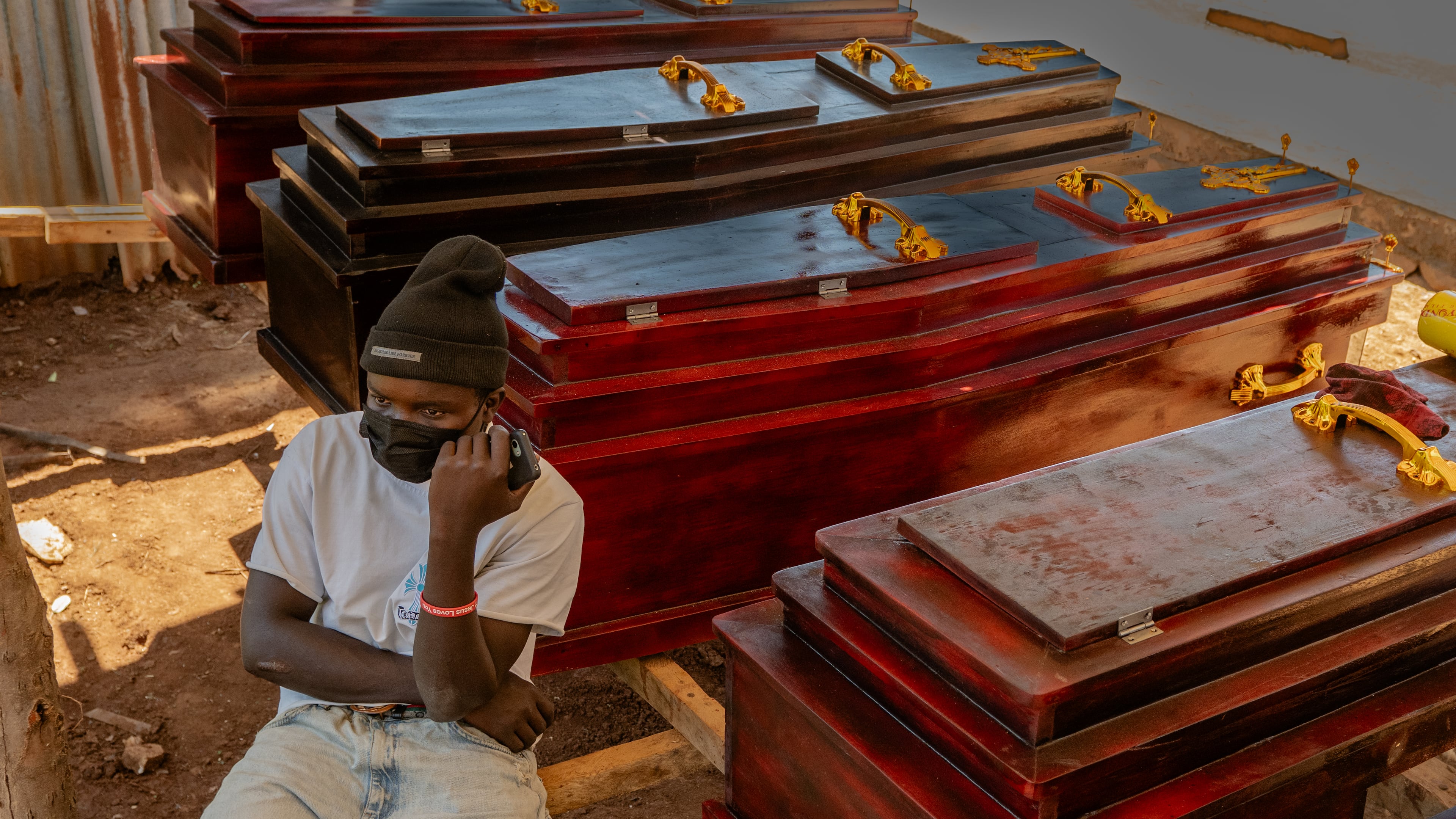 Djakisa Christian, 18, a funeral home manager, sits in front of coffins for sale at his shop in Bunia, Congo, Friday, May 22, 2026. (AP Photo/Moses Sawasawa)