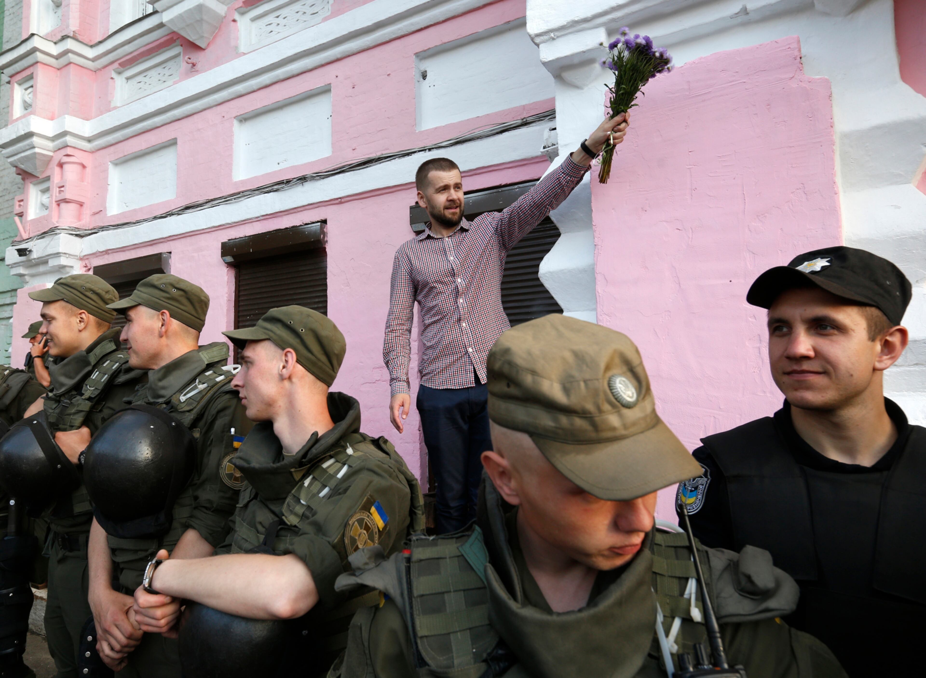 A gay rights activist holds a bunch of flowers behind servicemen of the National Guard line during the opening ceremony of the Pride Week in Kiev, Ukraine, Tuesday, June 13, 2017. (AP Photo/Sergei Chuzavkov)
