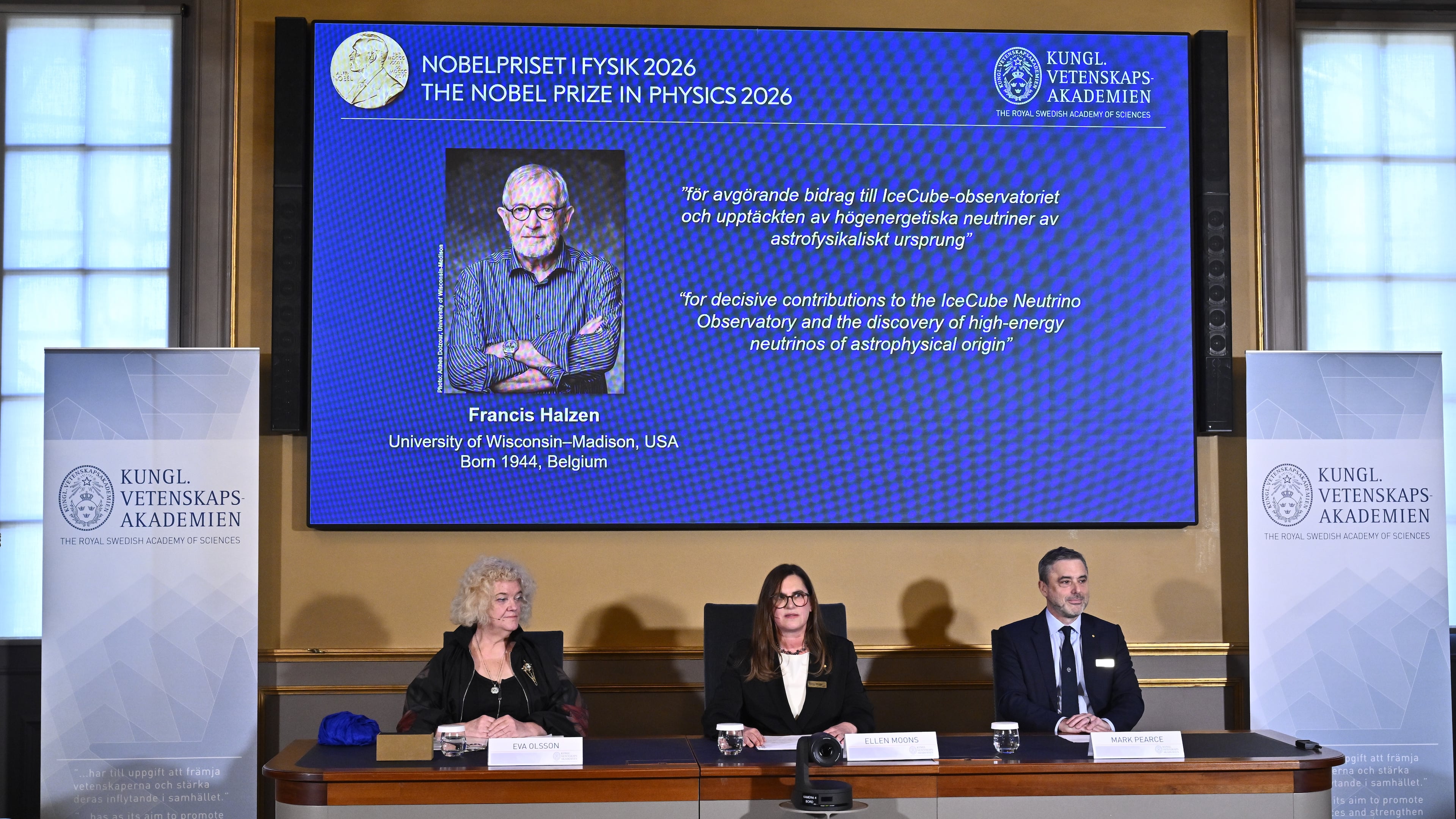 A portrait of Francis Halzen is shown on the screen as Eva Olsson, Ellen Moons, and Mark Pearce announce as the recipient of the 2026 Nobel Prize in Physics during a press conference at the Royal Swedish Academy of Sciences, Stockholm, Sweden, Oct. 6, 2026. (Christine Olsson/TT News Agency via AP)